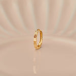 Close up of textured 18K gold nose ring standing upright on a soft beige background with subtle light reflections