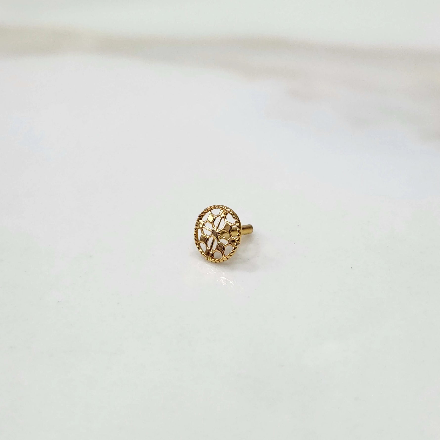 Front view of a small round 18K gold nose pin placed on a white background showcasing fine detailing and compact size