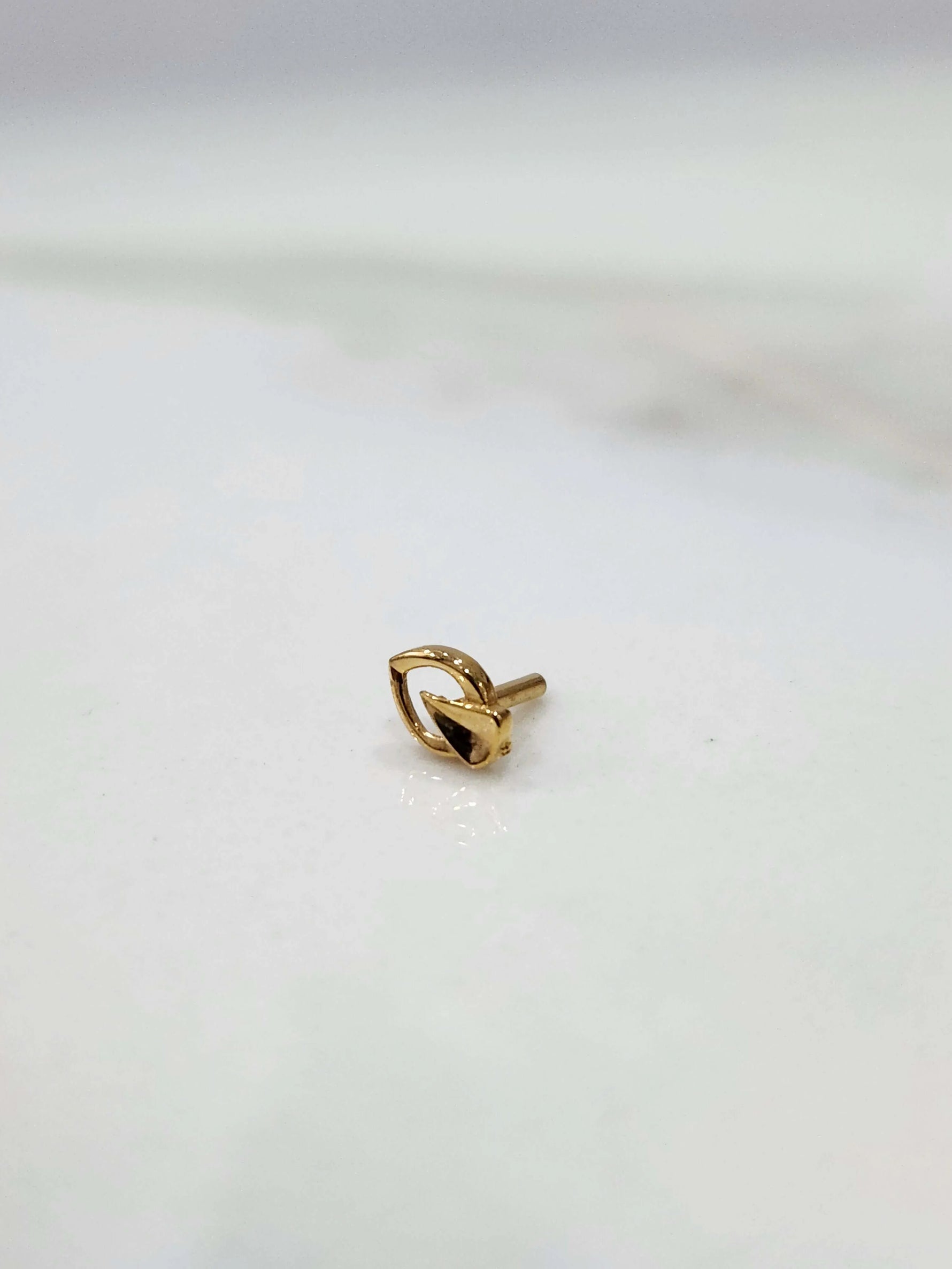Side view of a tiny 18K gold nose pin on a white surface highlighting its compact lightweight design