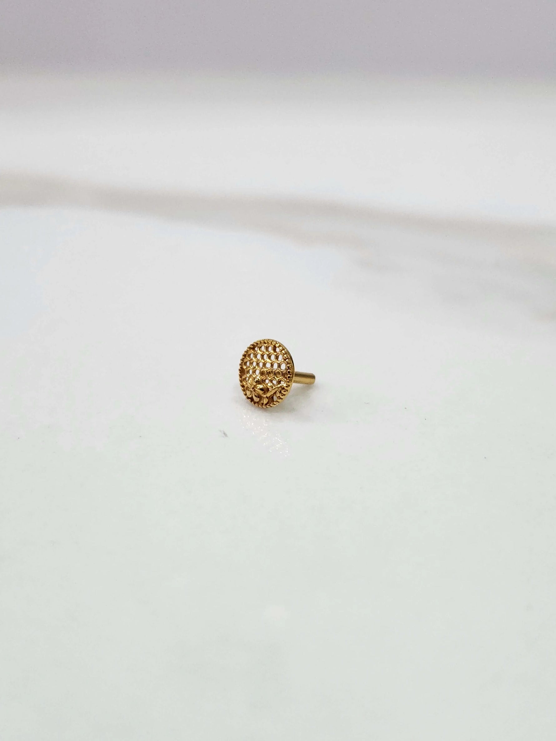 Side view of a small round 18K gold nose pin placed on a white surface showcasing its compact size and polished finish