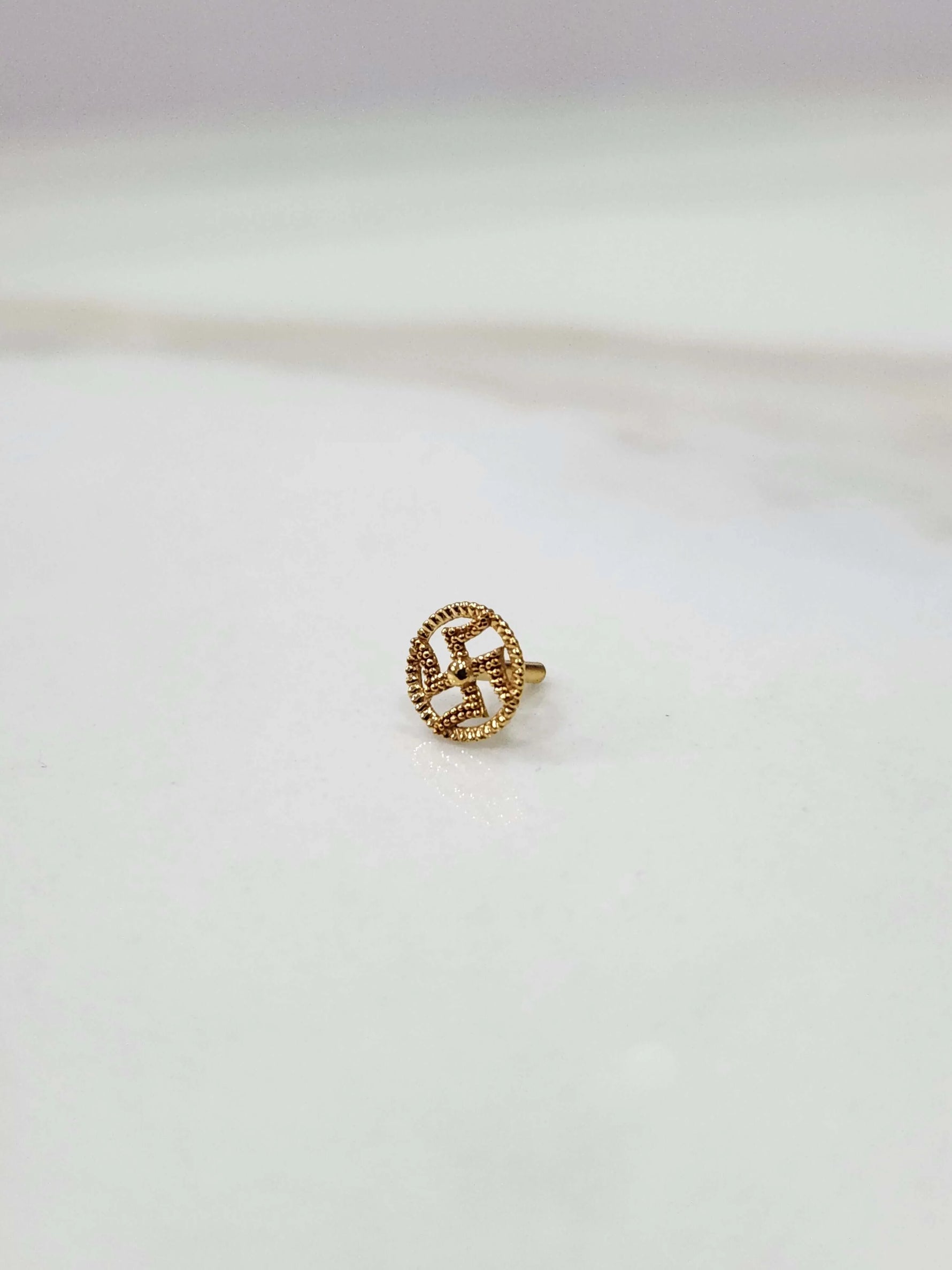 Close-up of a tiny 18K nose pin gold placed on a white surface showing fine detailing and compact finish
