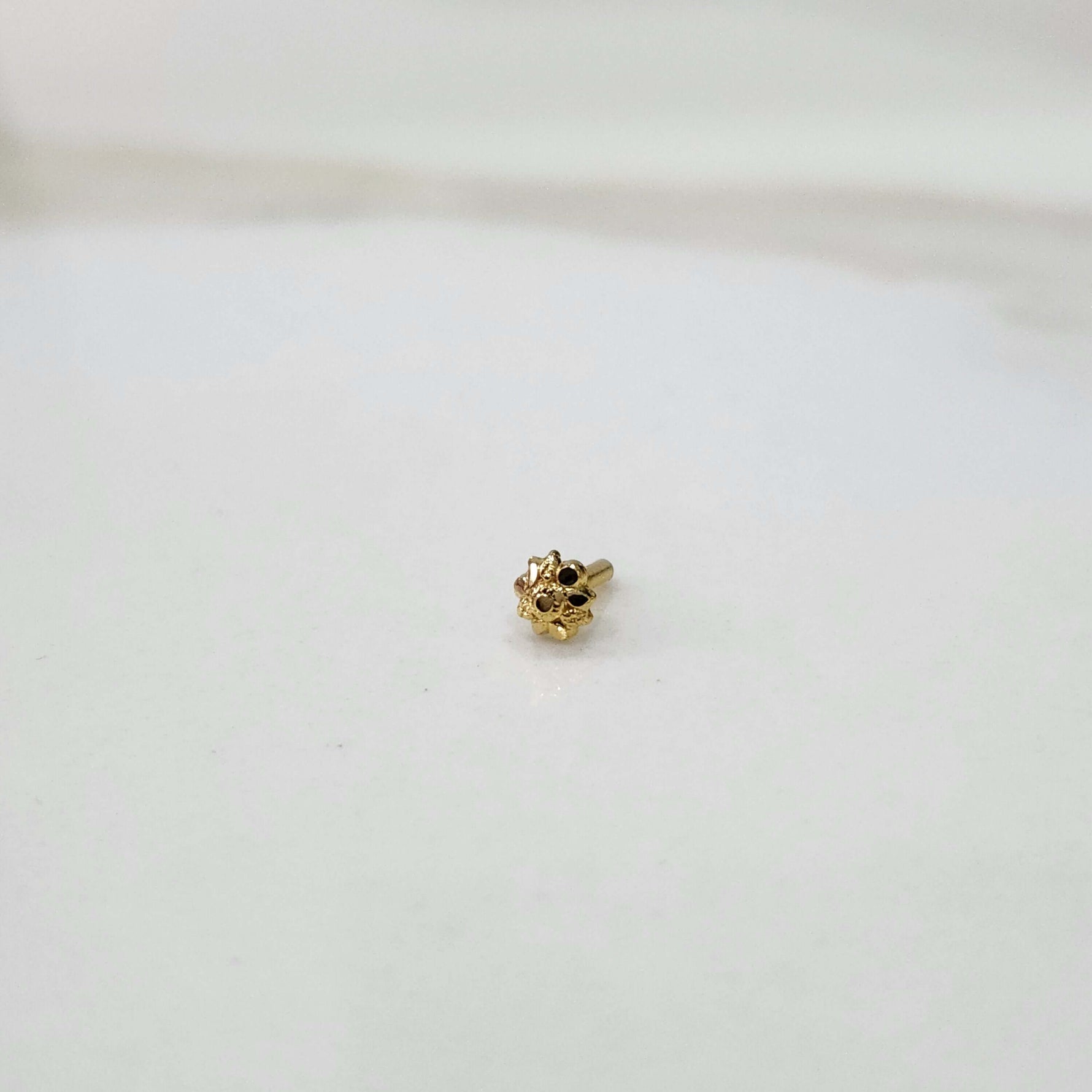 Slight angled view of a tiny gold nose pin on a white surface highlighting its fine detailing and subtle shine