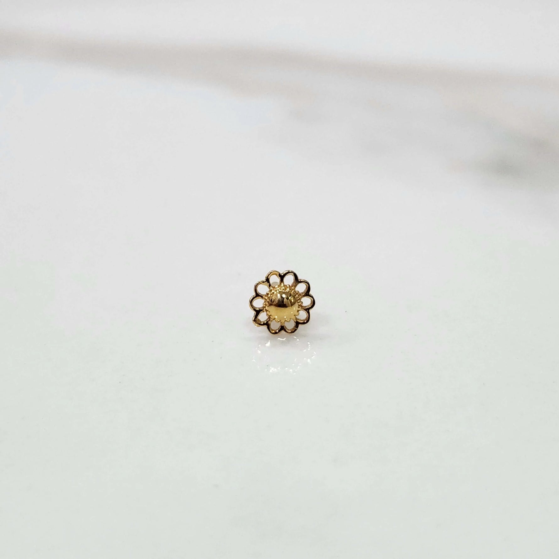 Front view of a tiny 18K gold nose pin placed on a white surface showing its compact size and fine craftsmanship