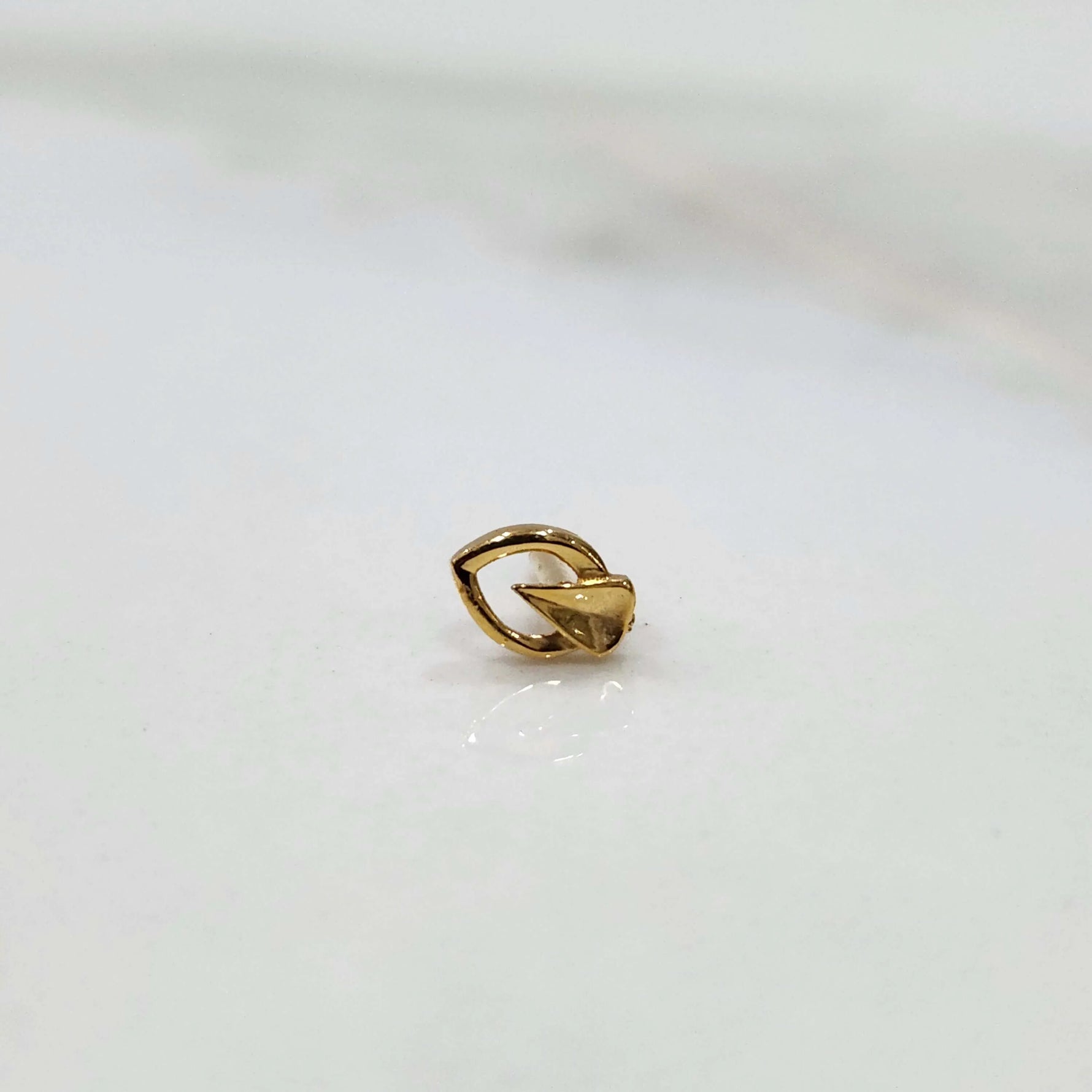 Close up of a small 18K gold nose pin placed on a white background showing fine detailing