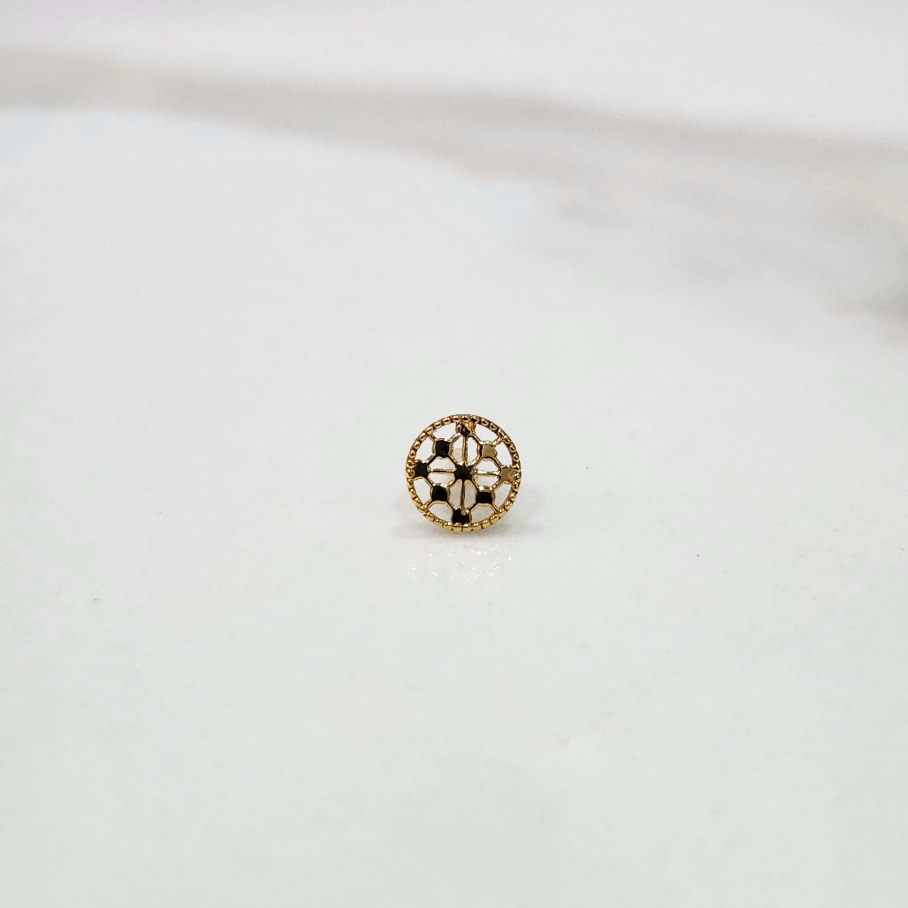 Slight angled view of a textured circular 18K gold nose pin on a white surface highlighting its polished finish and craftsmanship