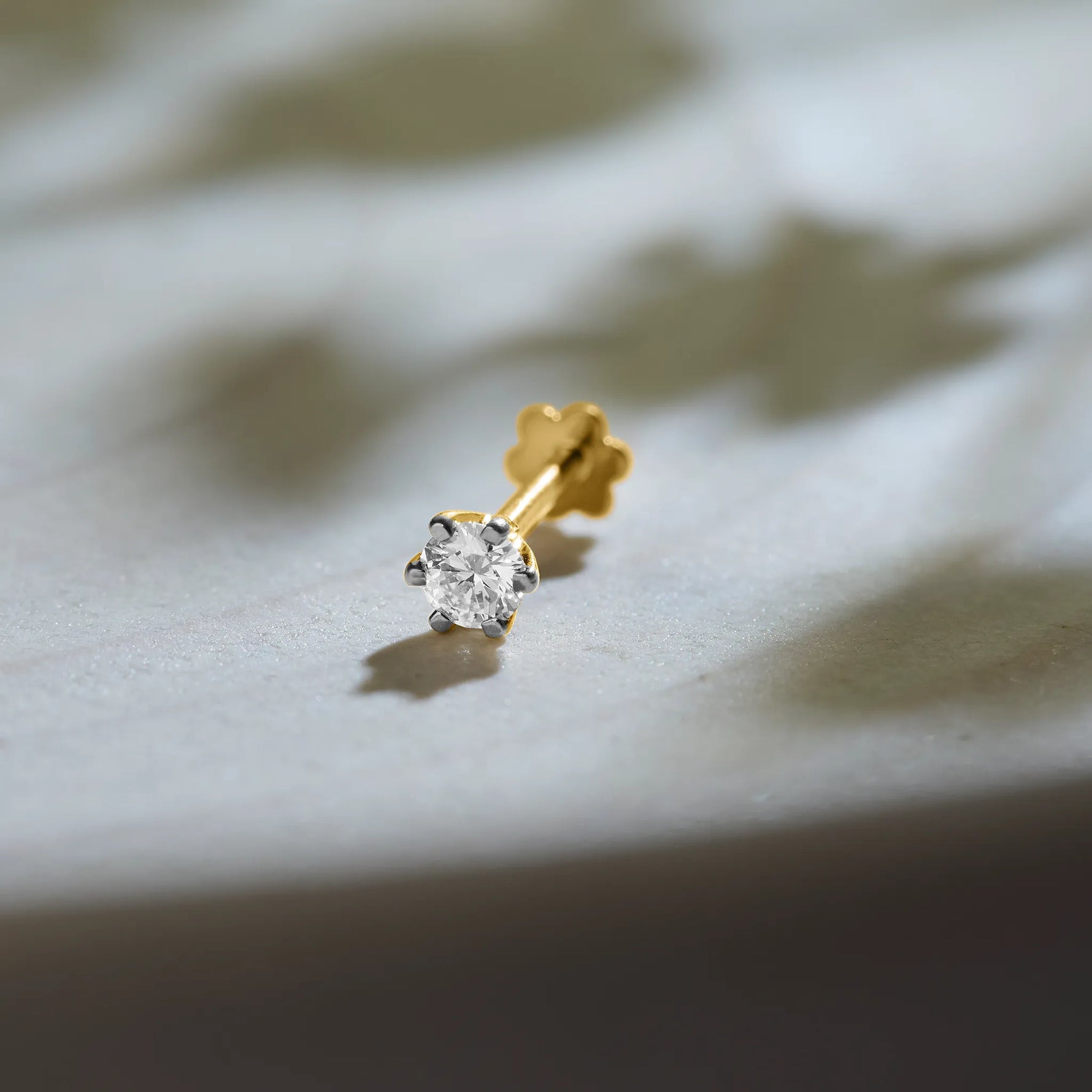 Diamond nose pin design from Kerala in gold with solitaire diamond on textured background