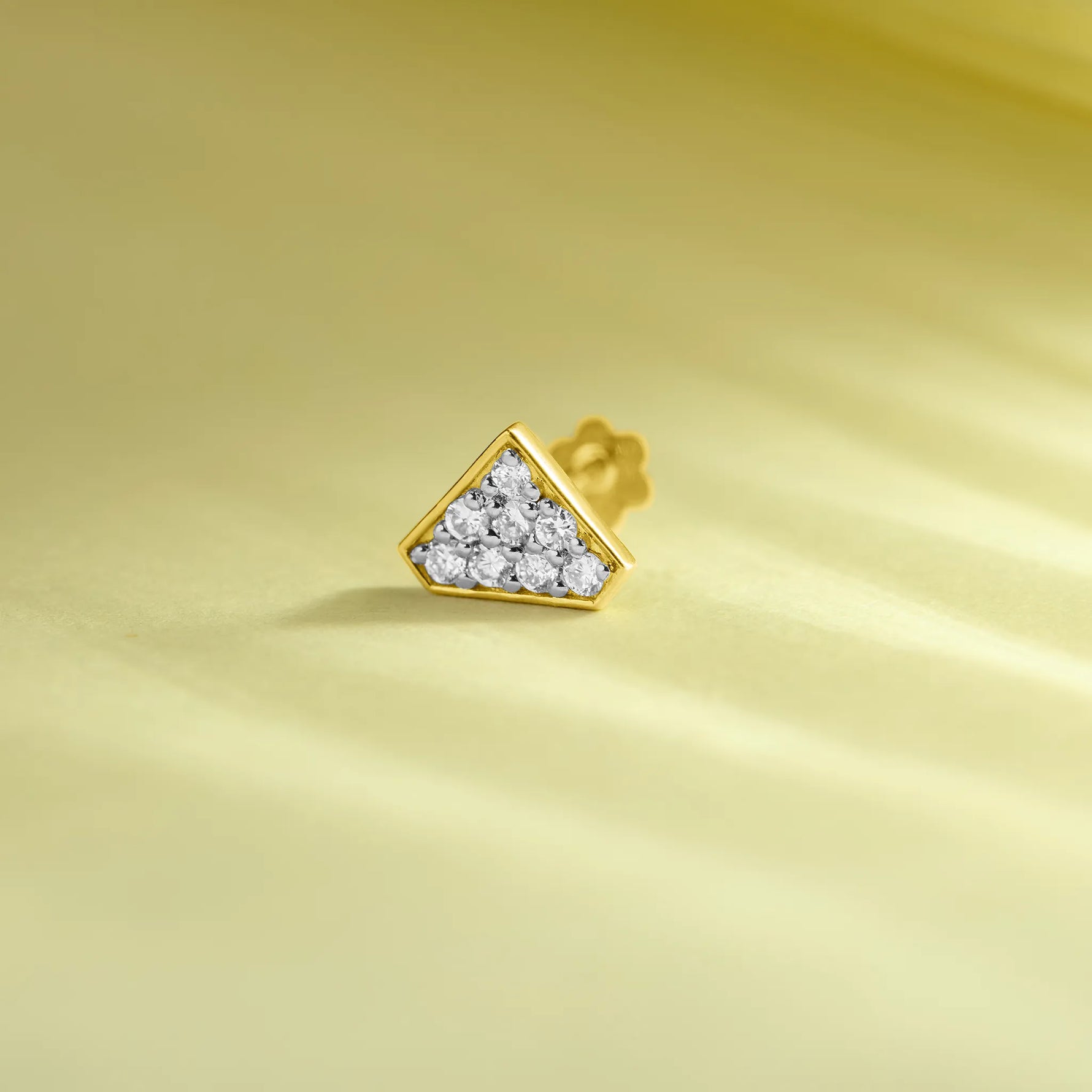 Gold triangle diamond nose pin product image on pastel yellow background