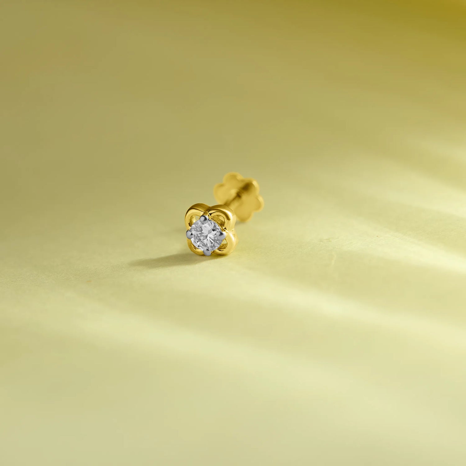 Elegant gold flower nose pin with a sparkling round stone placed on a soft pastel green background.