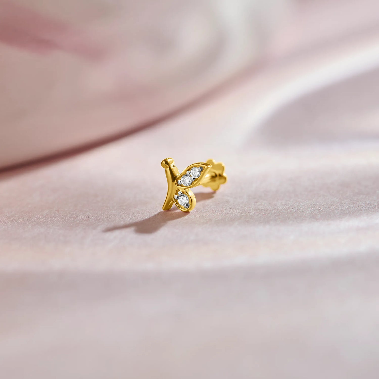 Nose pin of gold with butterfly inspired diamond design on soft pink fabric background