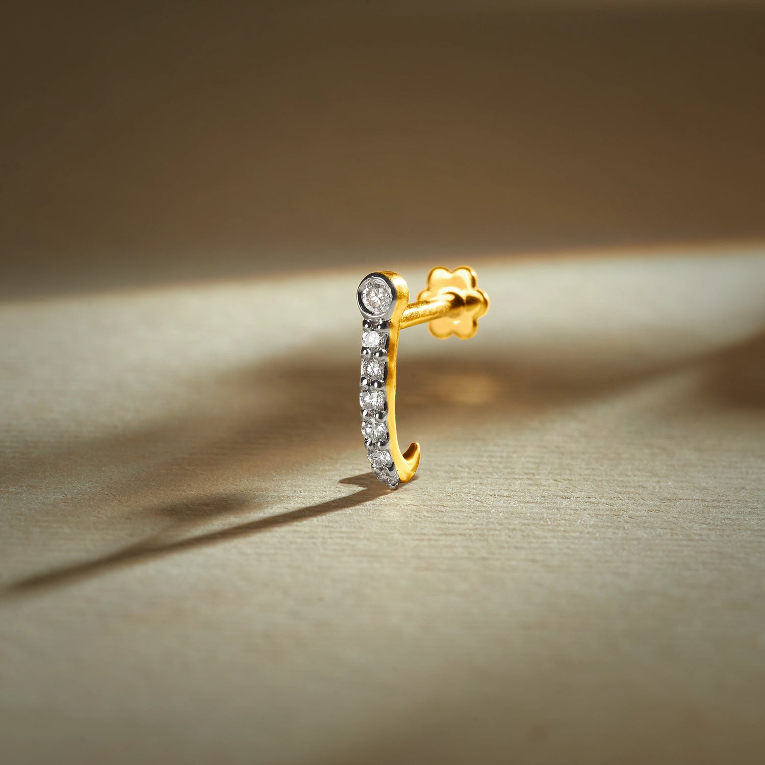 J type nose pin gold with curved hoop design featuring a row of sparkling stones set in a polished gold base on a soft neutral background