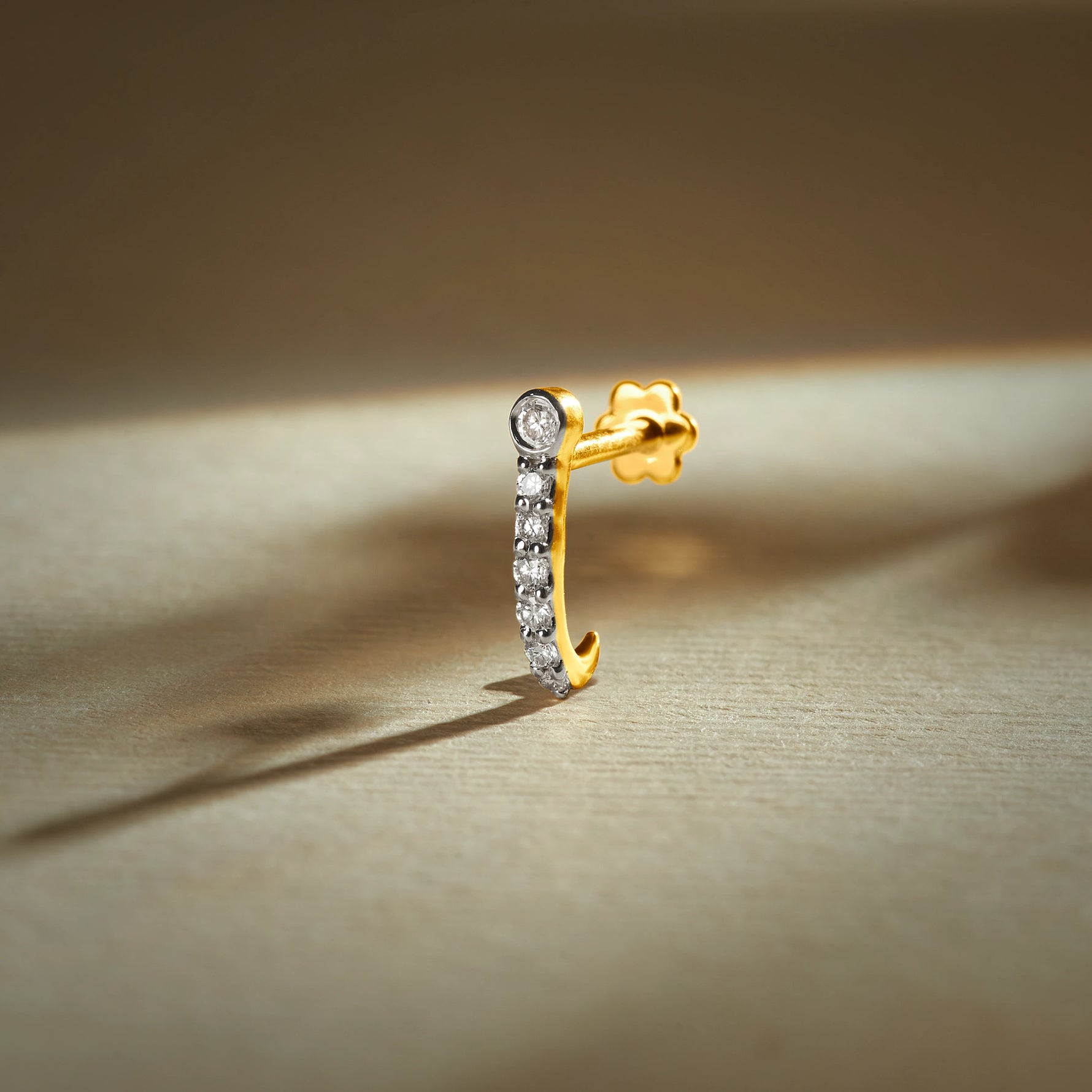 J type nose pin gold with curved hoop design featuring a row of sparkling stones set in a polished gold base on a soft neutral background