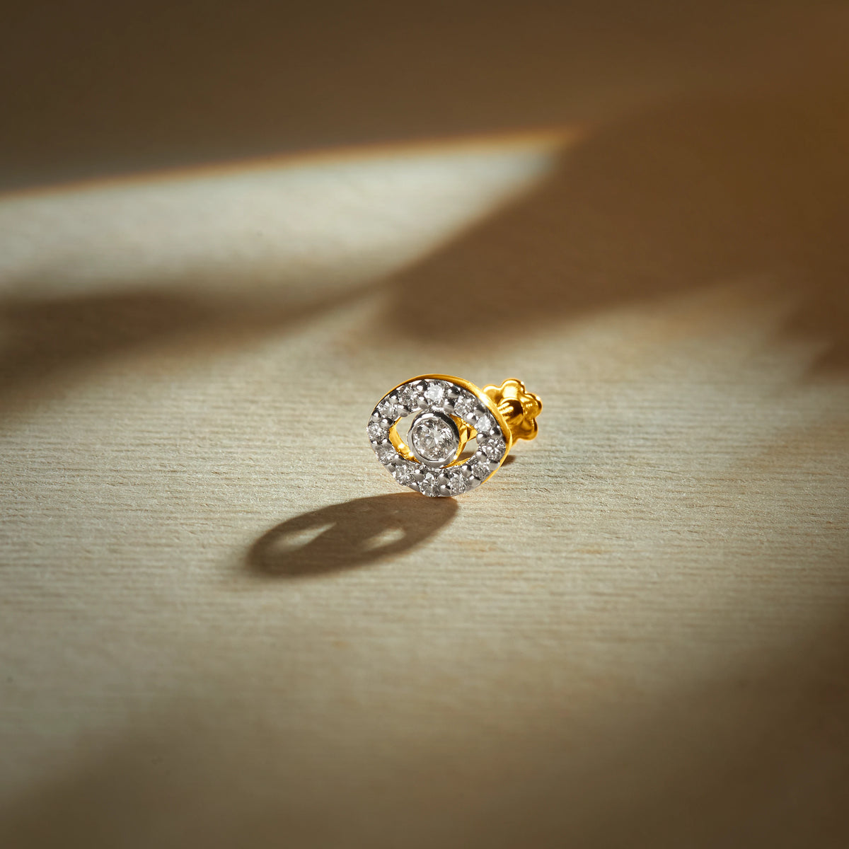 Gold nose pin with circular halo design featuring a central stone surrounded by sparkling accents set in a polished gold base on a soft neutral background