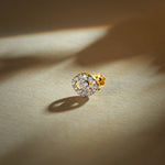 Gold nose pin with circular halo design featuring a central stone surrounded by sparkling accents set in a polished gold base on a soft neutral background