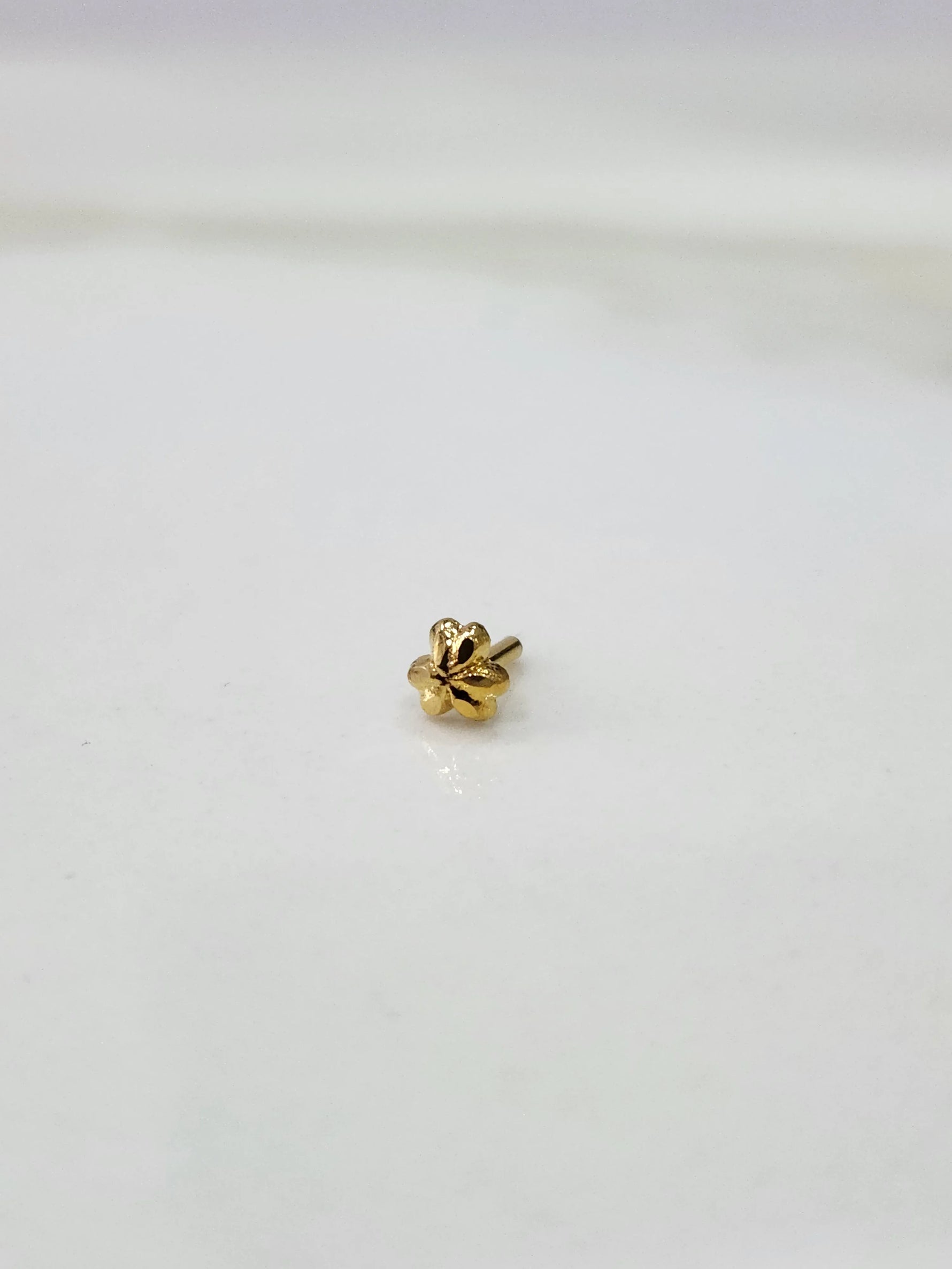 Side angle view of floral 18K gold nose pin on a white surface highlighting its compact and lightweight design