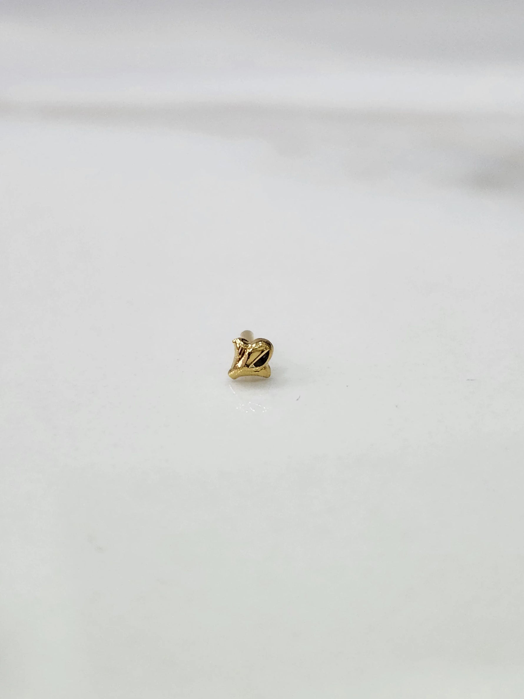Side view of lightweight 18K gold nose pin on a white surface highlighting compact design and fine detailing