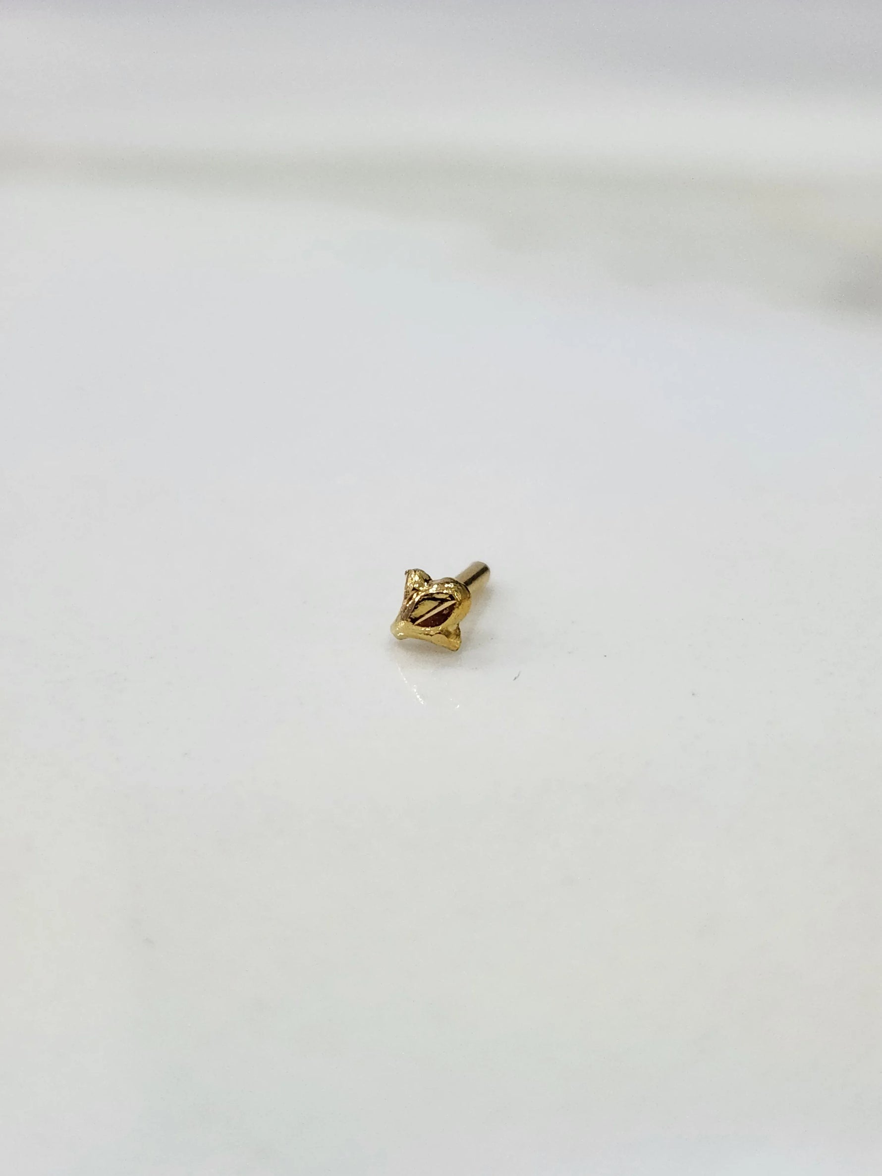 Front view of minimal 18K gold nose pin on a white background showing its petite size