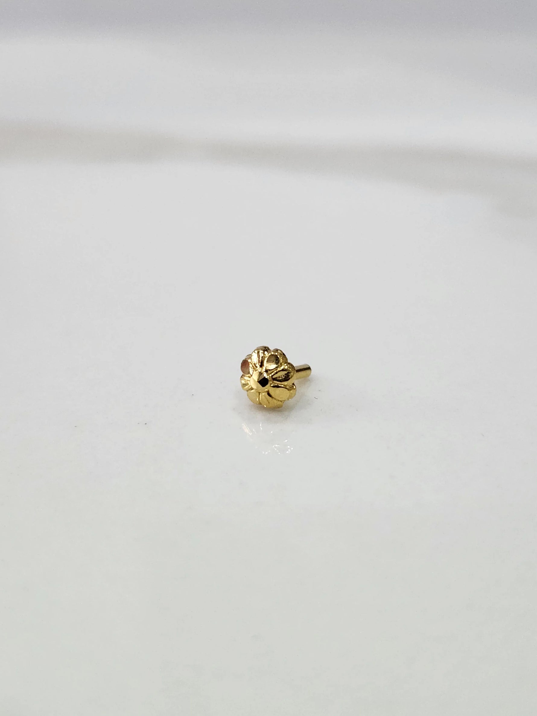 Close-up of a tiny gold nose pin placed on a white marble surface