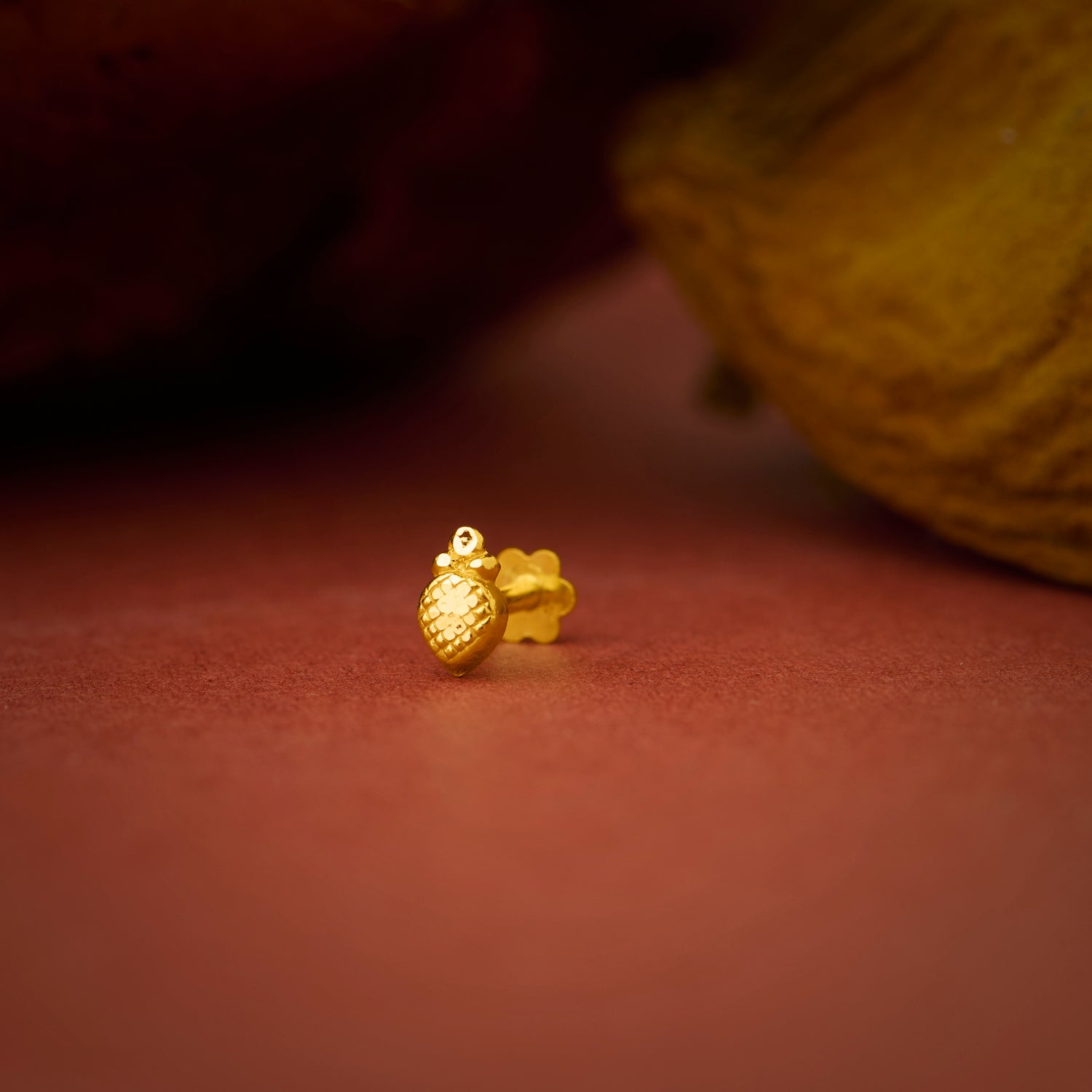 Close up of a small gold nose pin placed on a warm brown textured surface highlighting its smooth polished finish