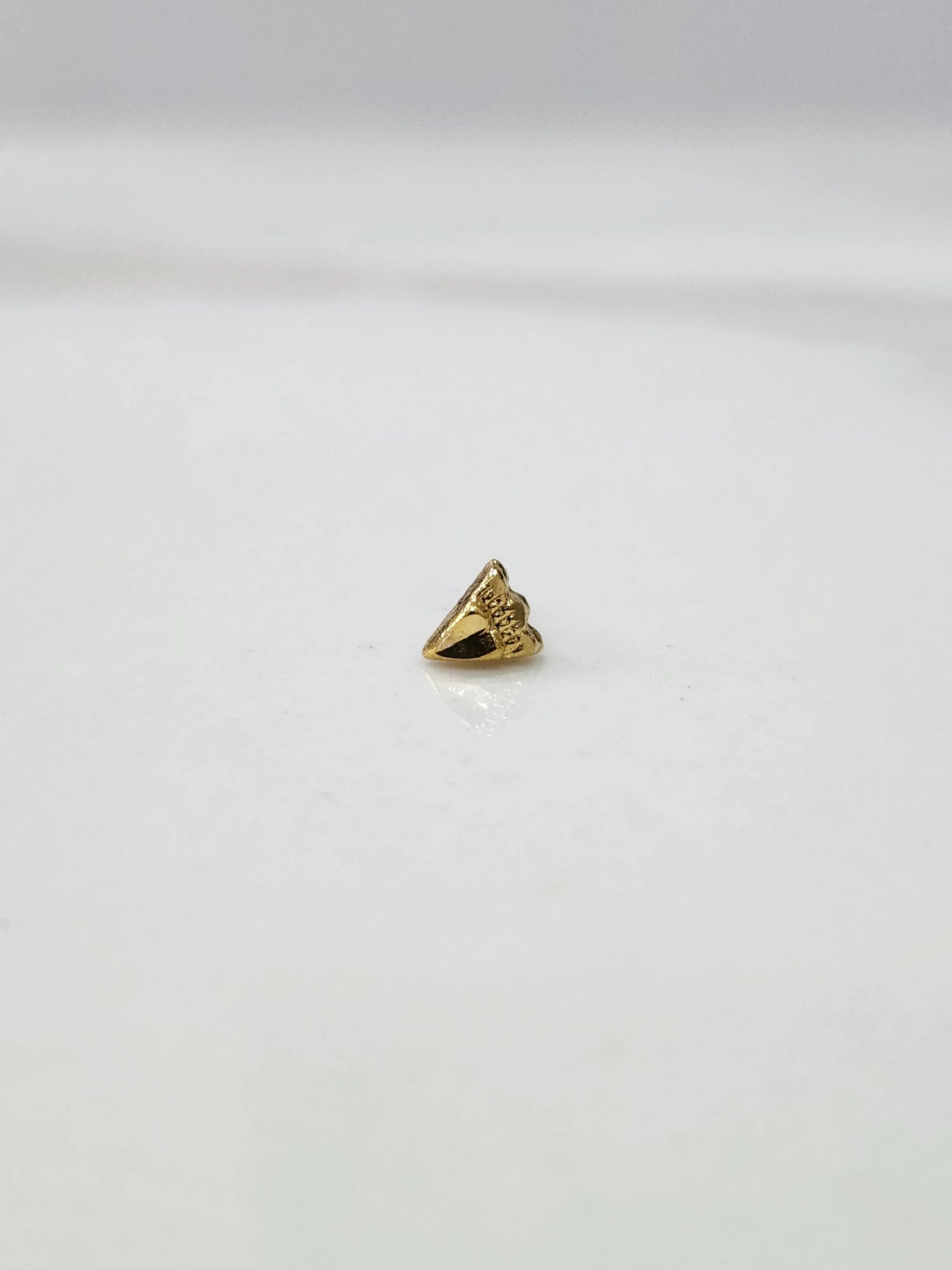 Side view of a tiny gold nose pin on a white surface highlighting its pointed design and subtle shine