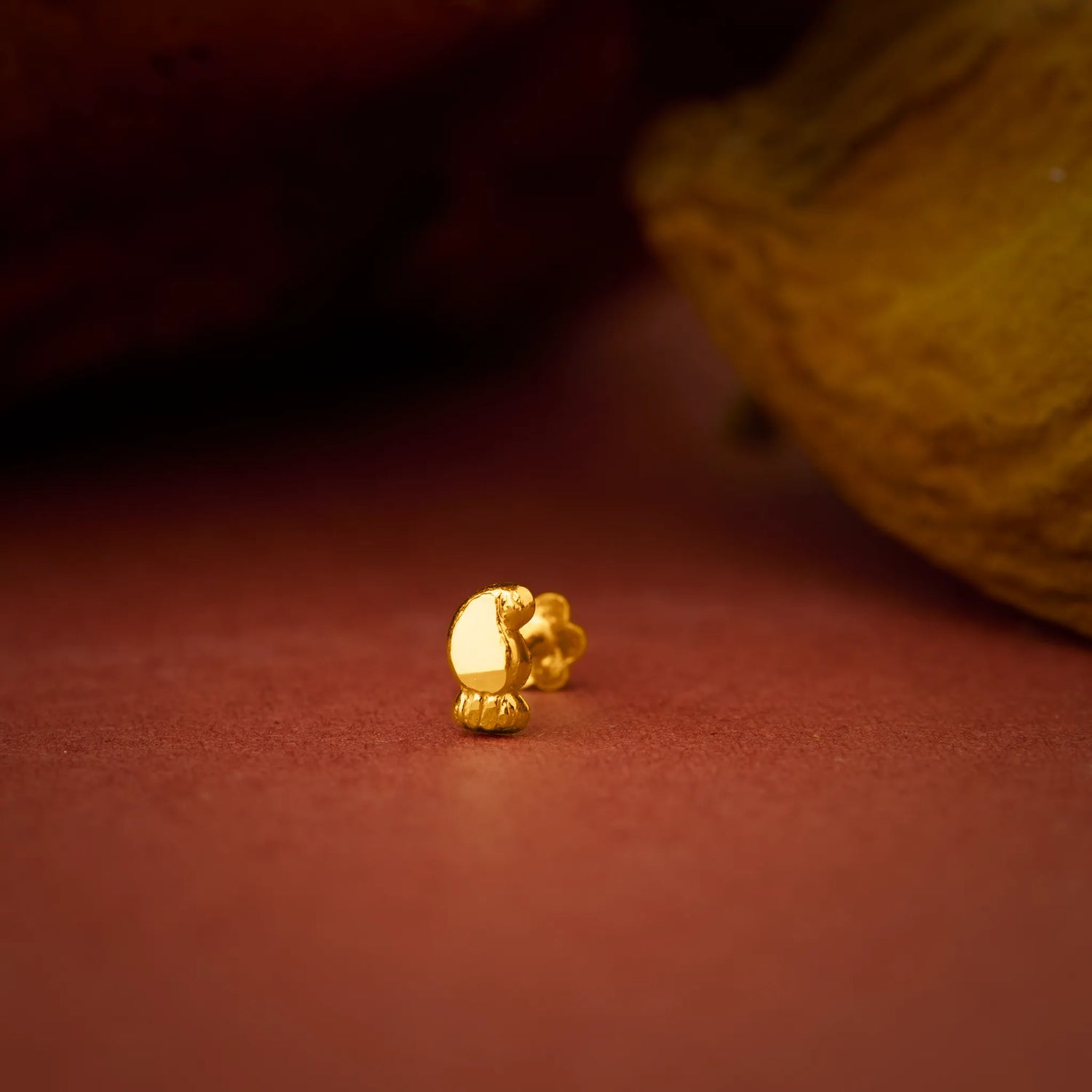 Close up of a small gold nose pin placed on a warm brown surface highlighting its polished finish and delicate design