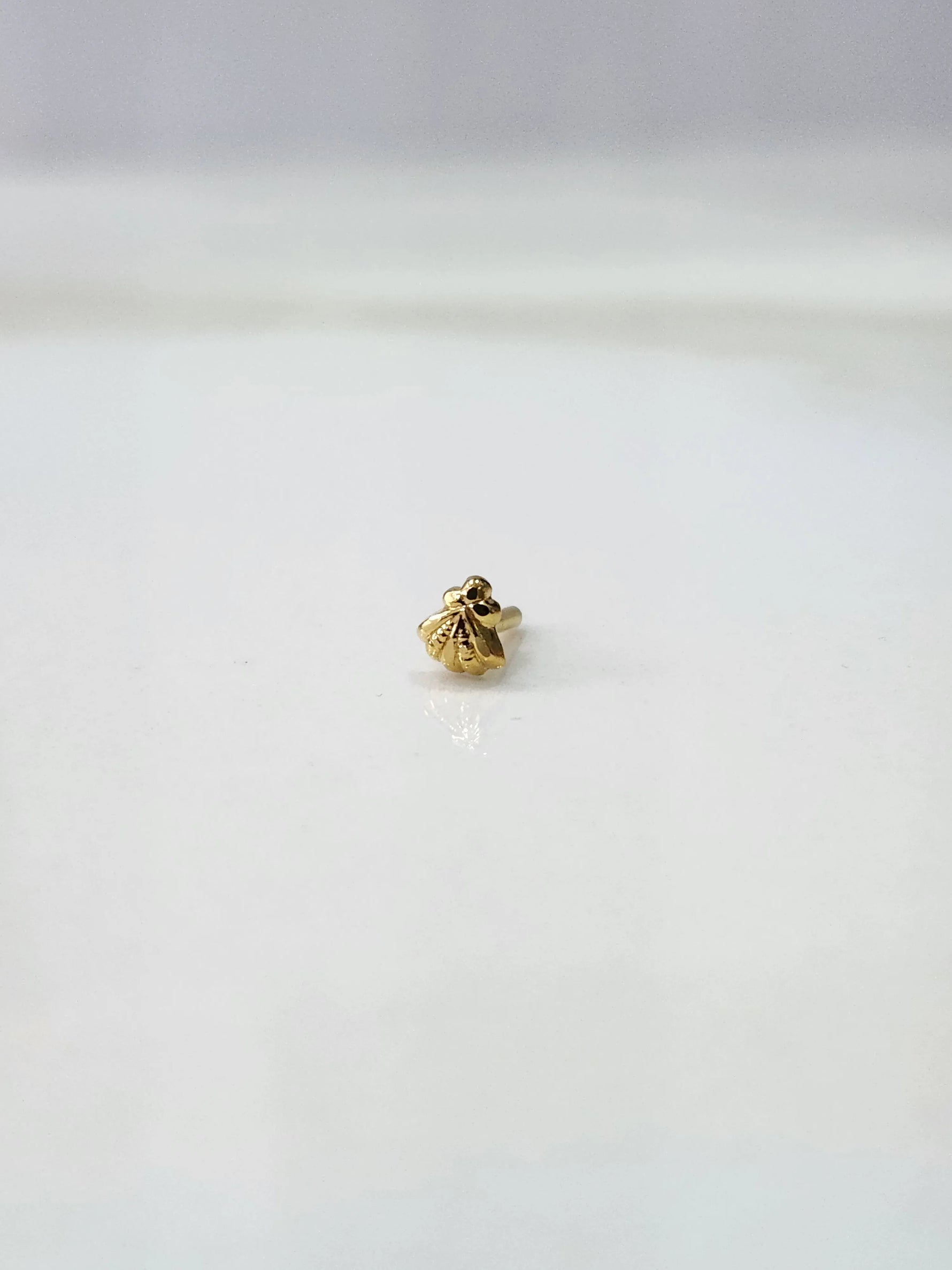 Side view of a delicate gold nose pin on a white surface highlighting its neat finish and lightweight form