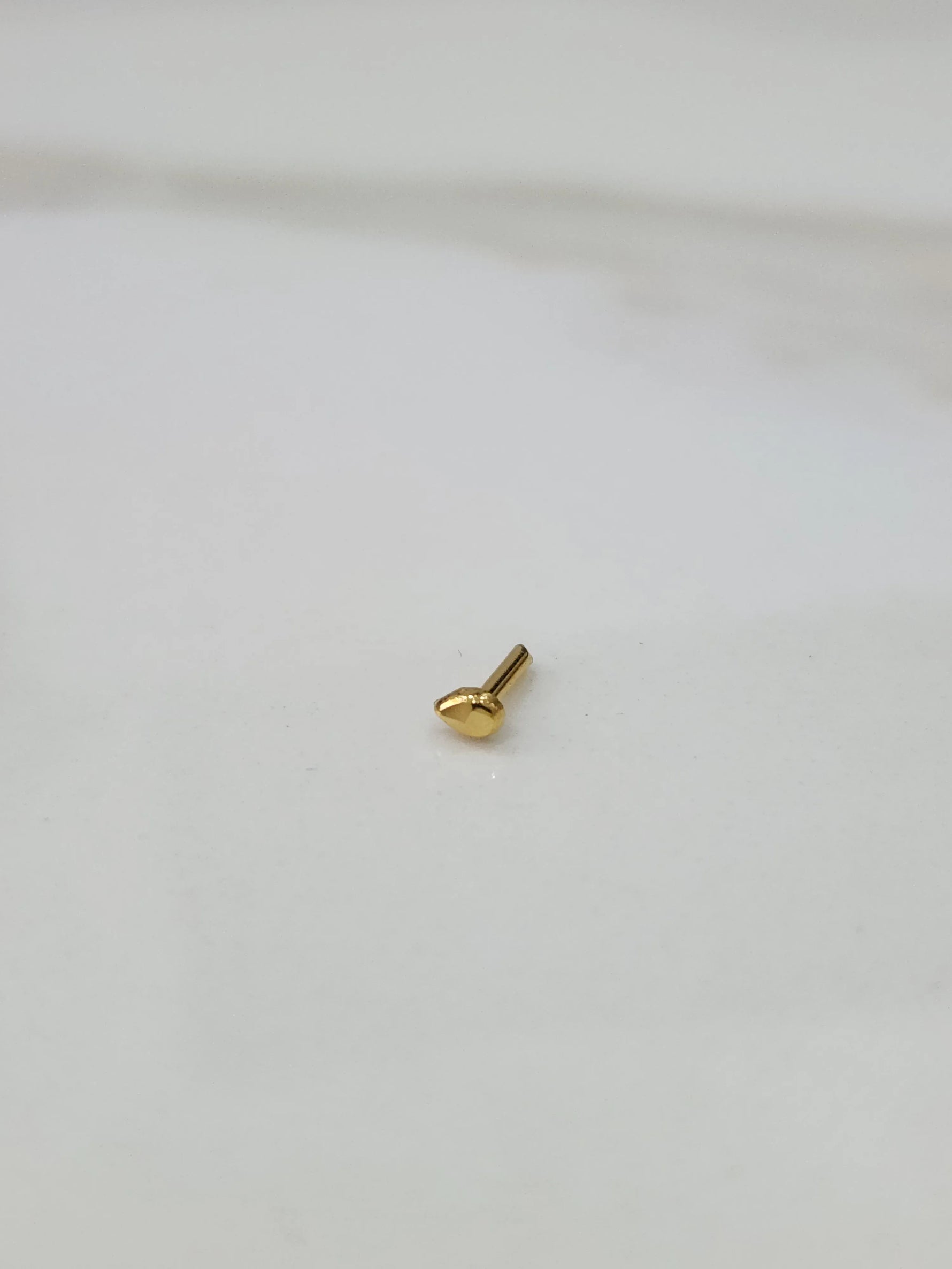 Side angle view of small teardrop gold nose pin highlighting compact and refined design