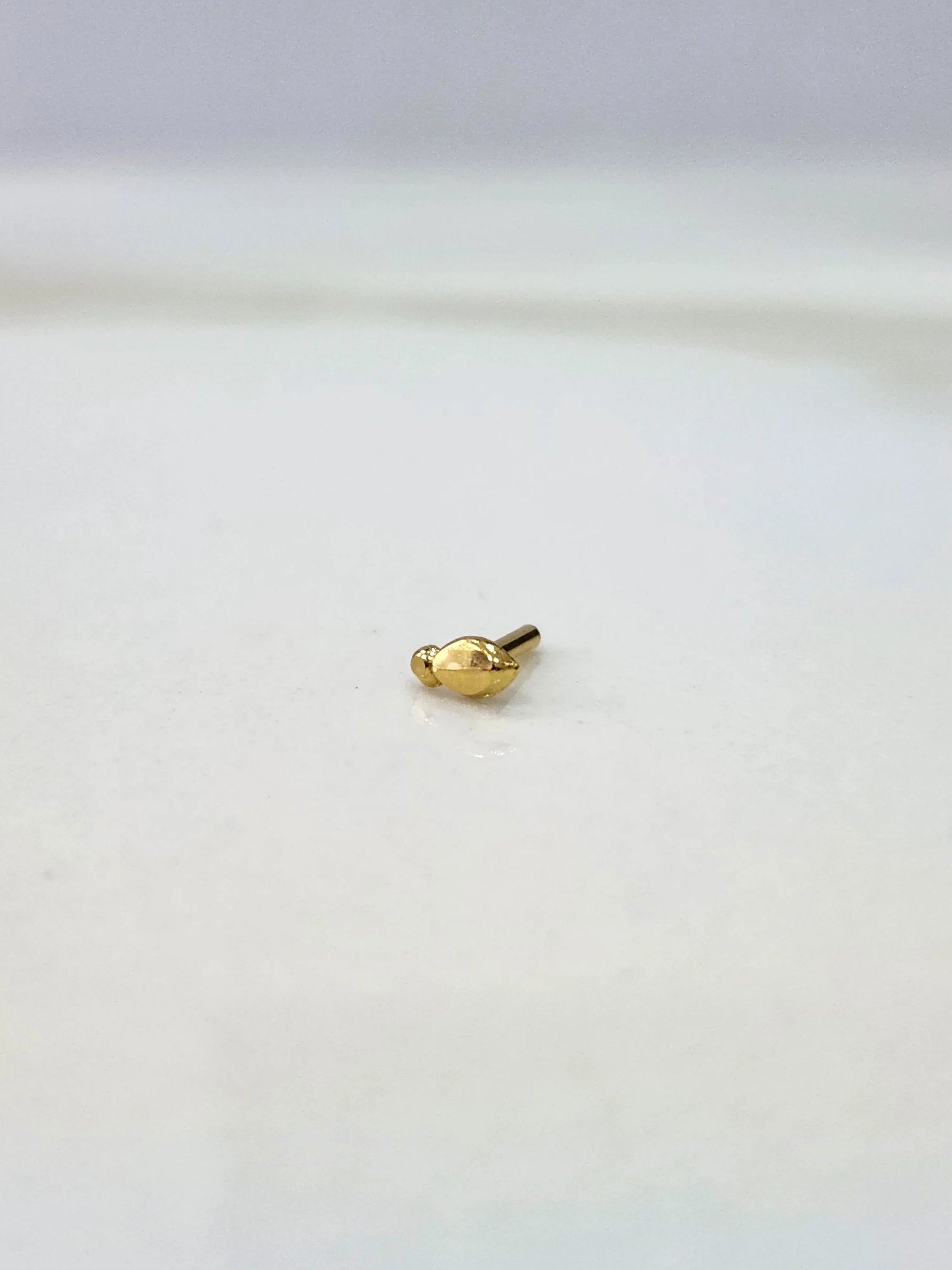 Front view of a small gold nose pin on a white background emphasizing its delicate design