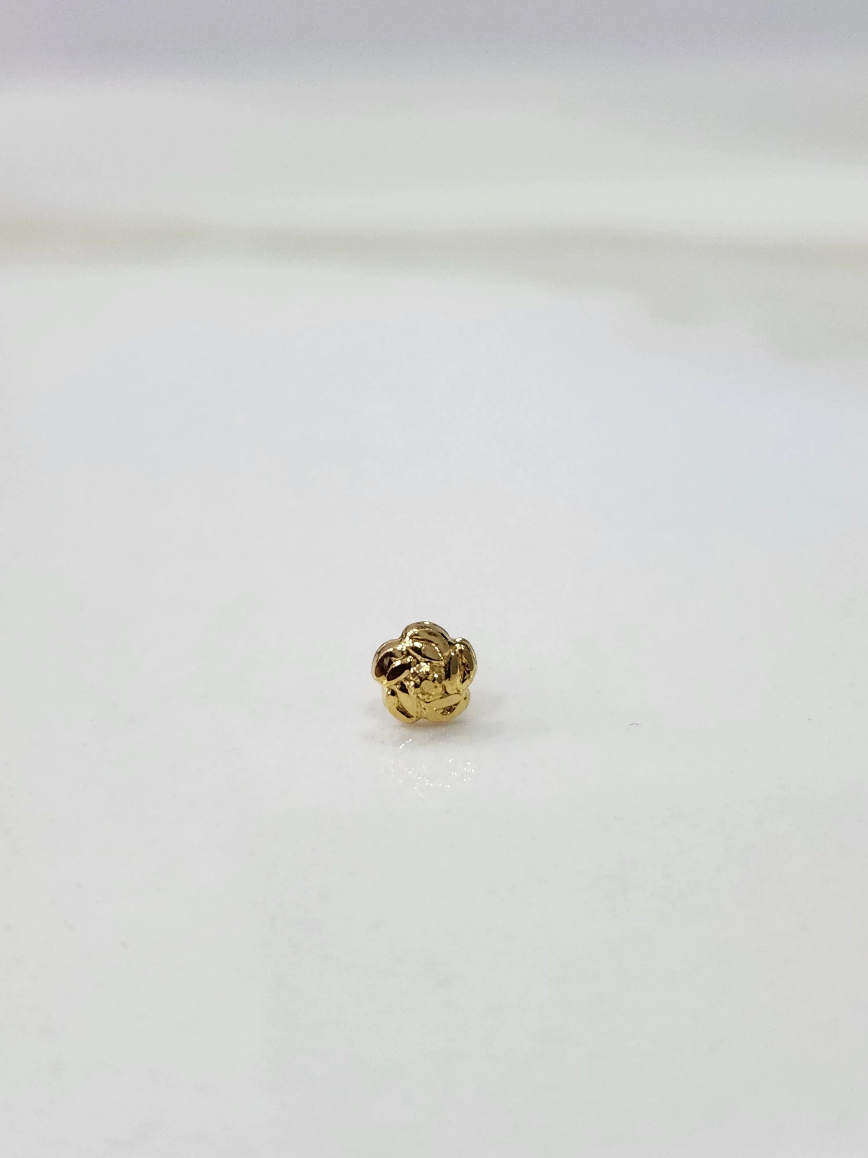 Side view of a tiny gold nose pin on a white surface displaying its lightweight build and subtle shine