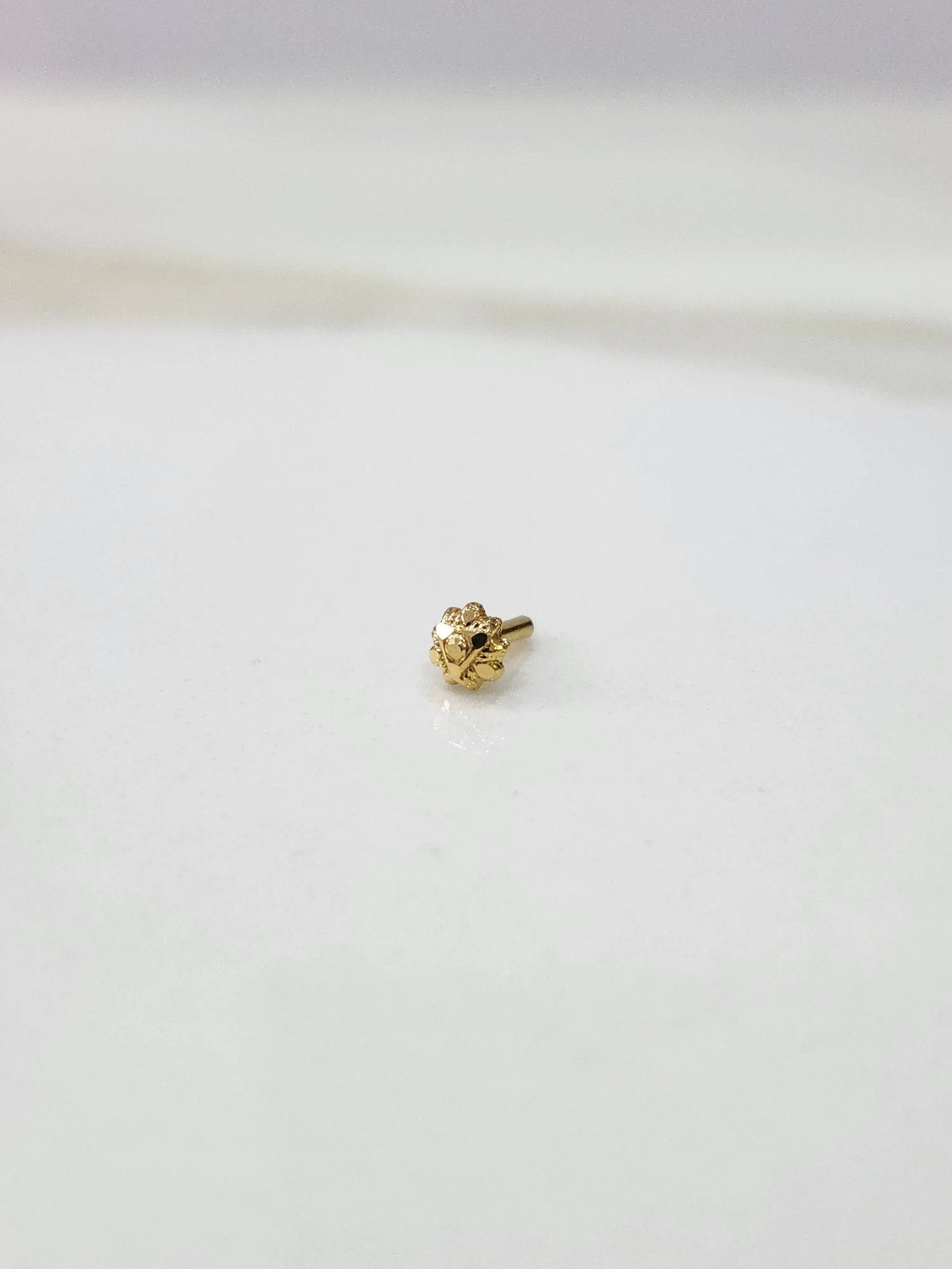 Small gold nose pin placed on a white background displaying fine detailing and compact proportions