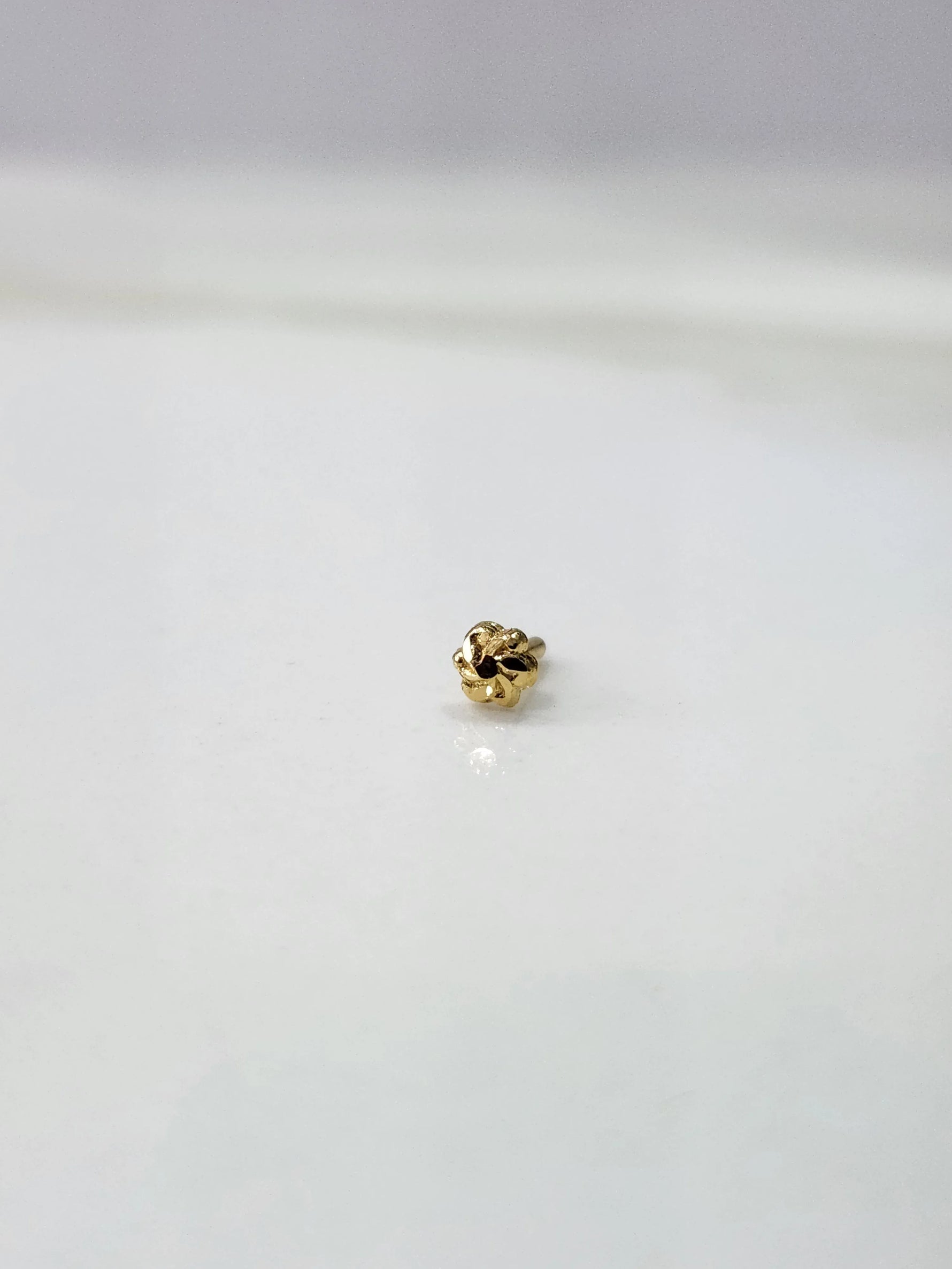 Front view of a tiny 18K gold nose pin on a white background showing its compact size and fine detailing