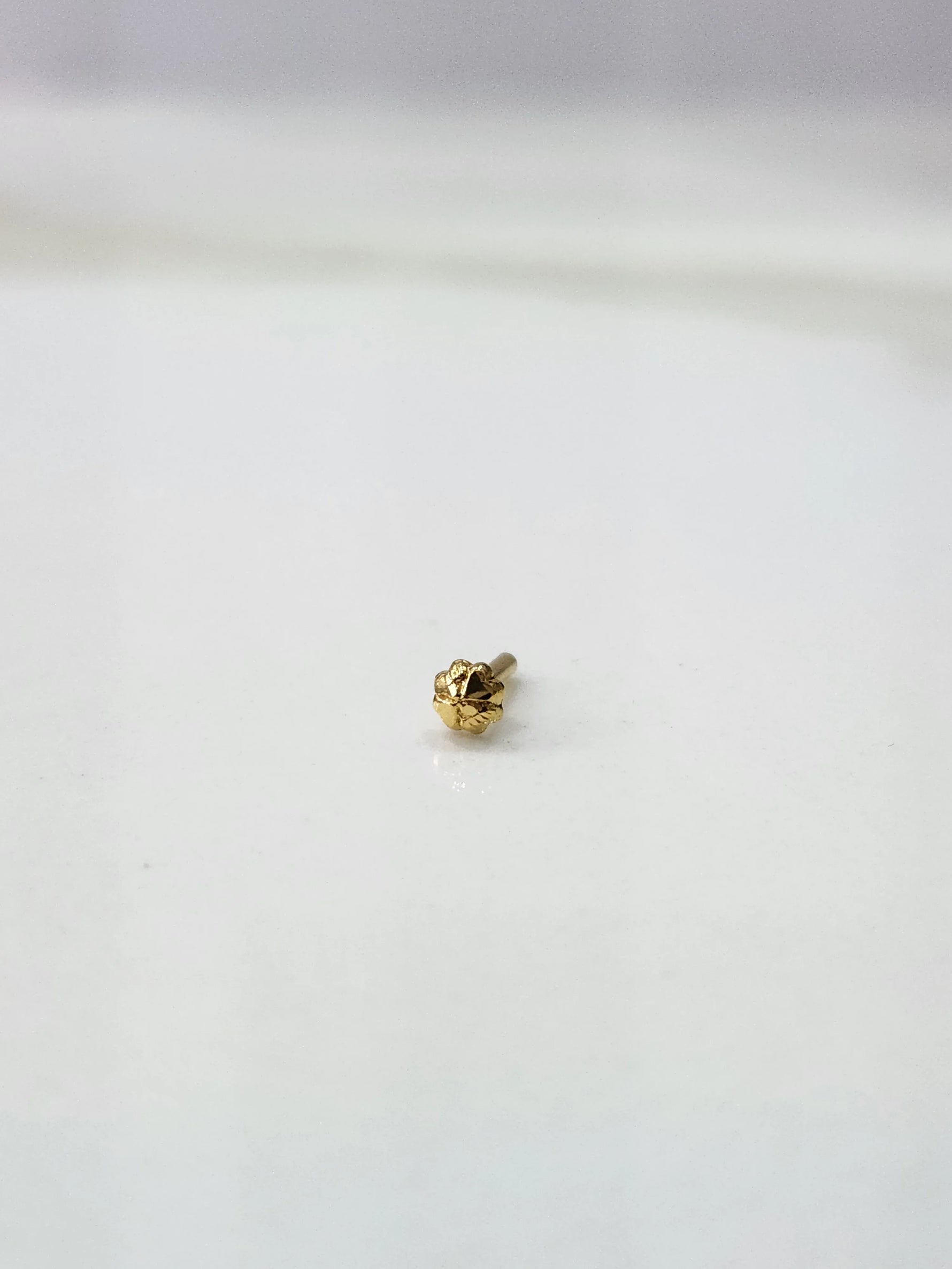 Front view of a delicate gold nose pin placed on a white background showing fine craftsmanship