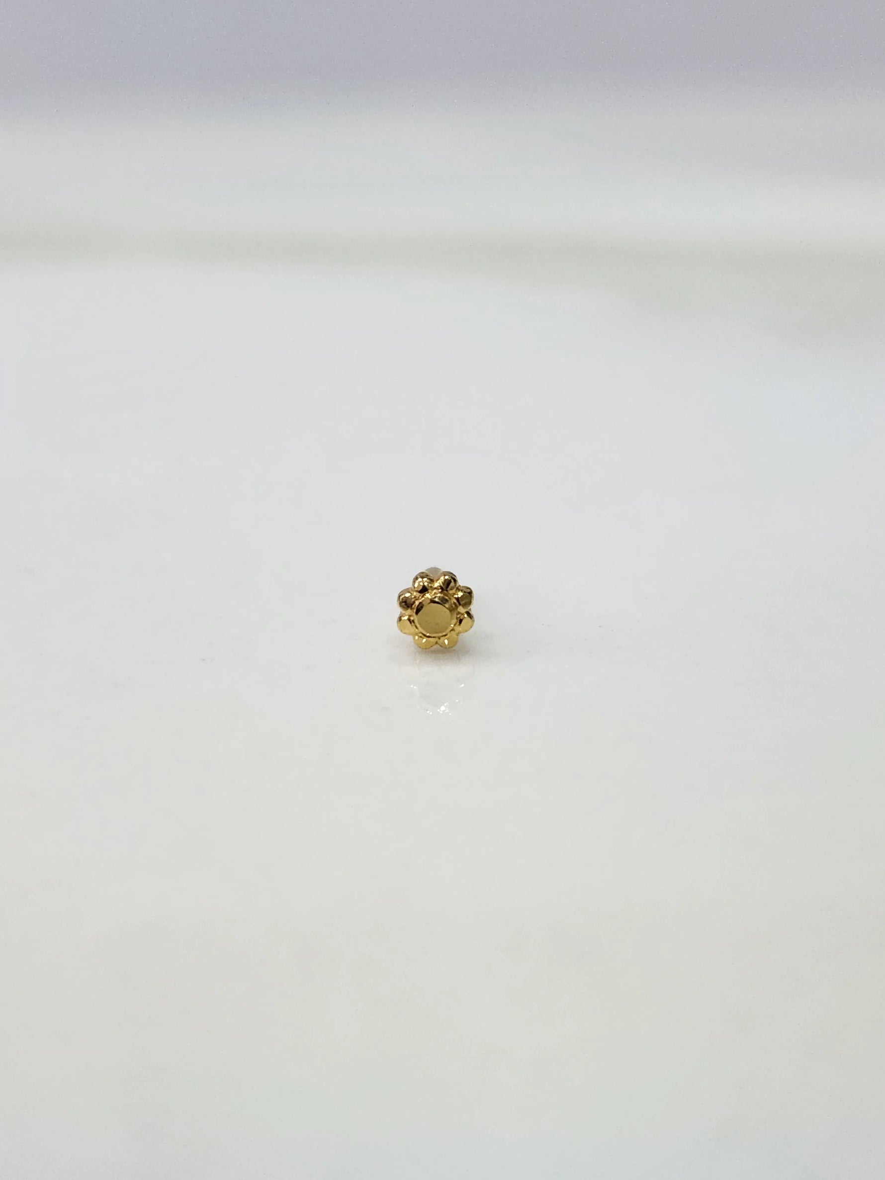 Side view of a tiny gold nose pin on a white surface emphasizing fine craftsmanship