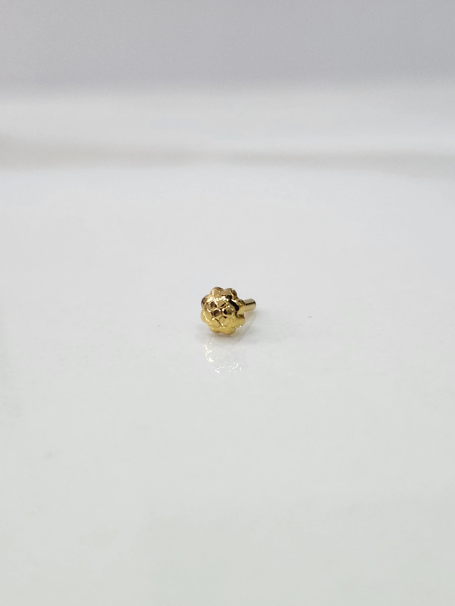 Front view of a small gold nose pin placed on a white background highlighting delicate detailing
