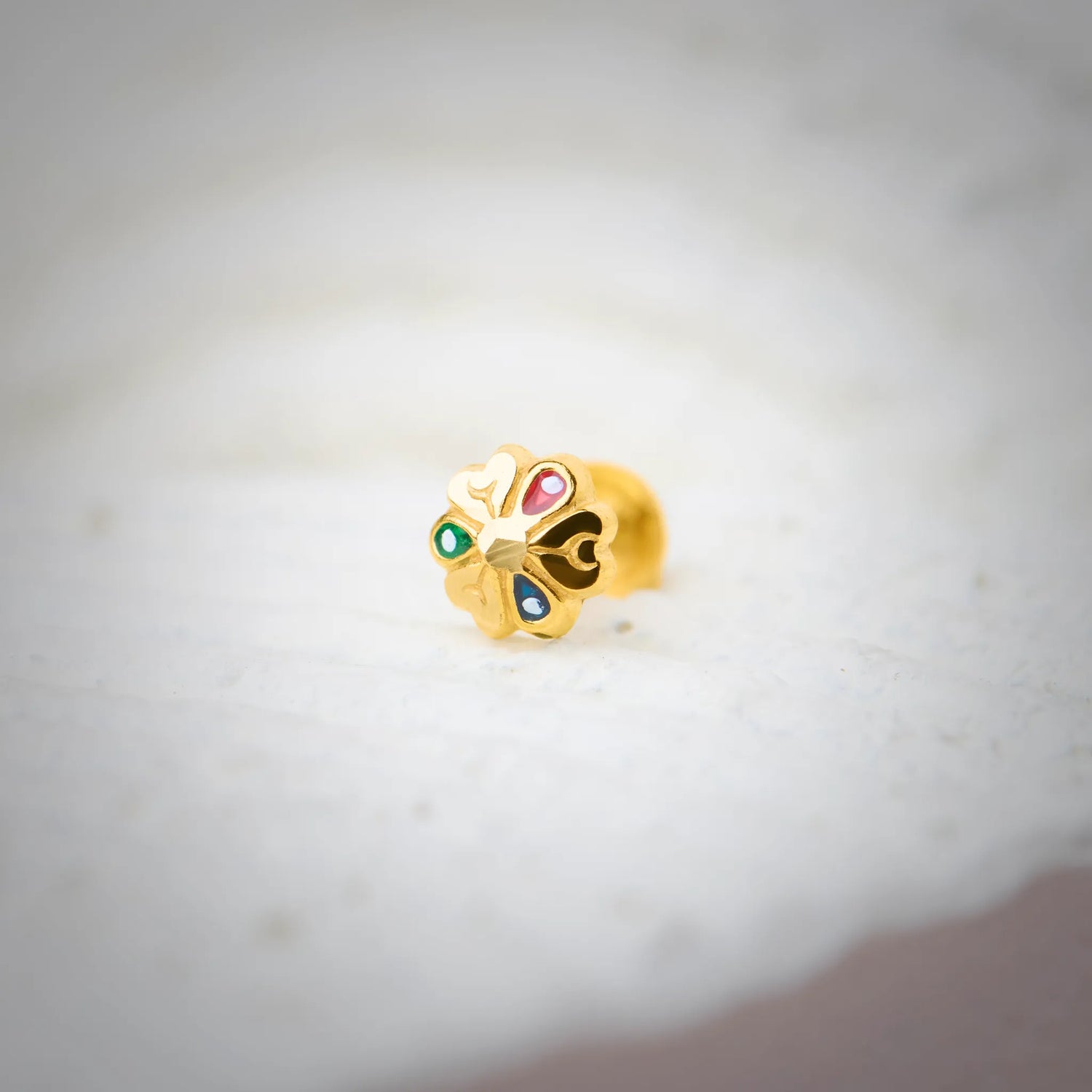 Close-up of multicolour stone 18K nose pin gold placed on a soft white surface highlighting its vibrant detailing