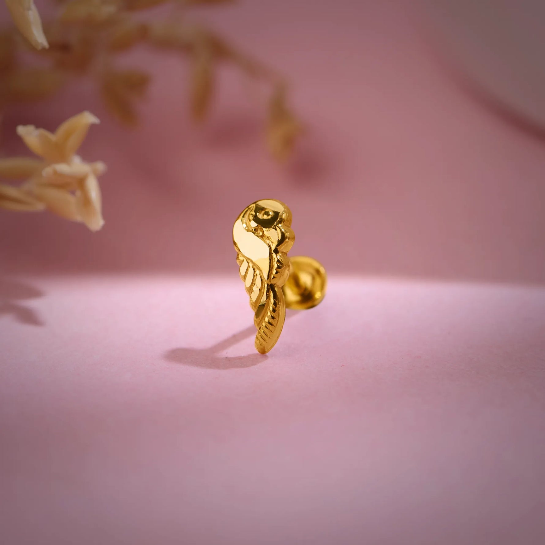 Artistic close-up of a designer 18K nose pin gold on a soft pink background