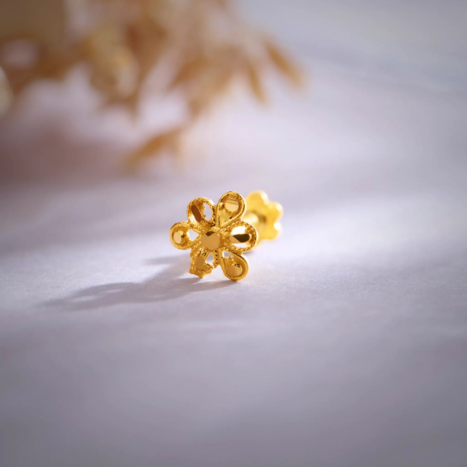 Close up of a floral 18K nose pin gold placed on a soft white surface highlighting intricate design and polished finish
