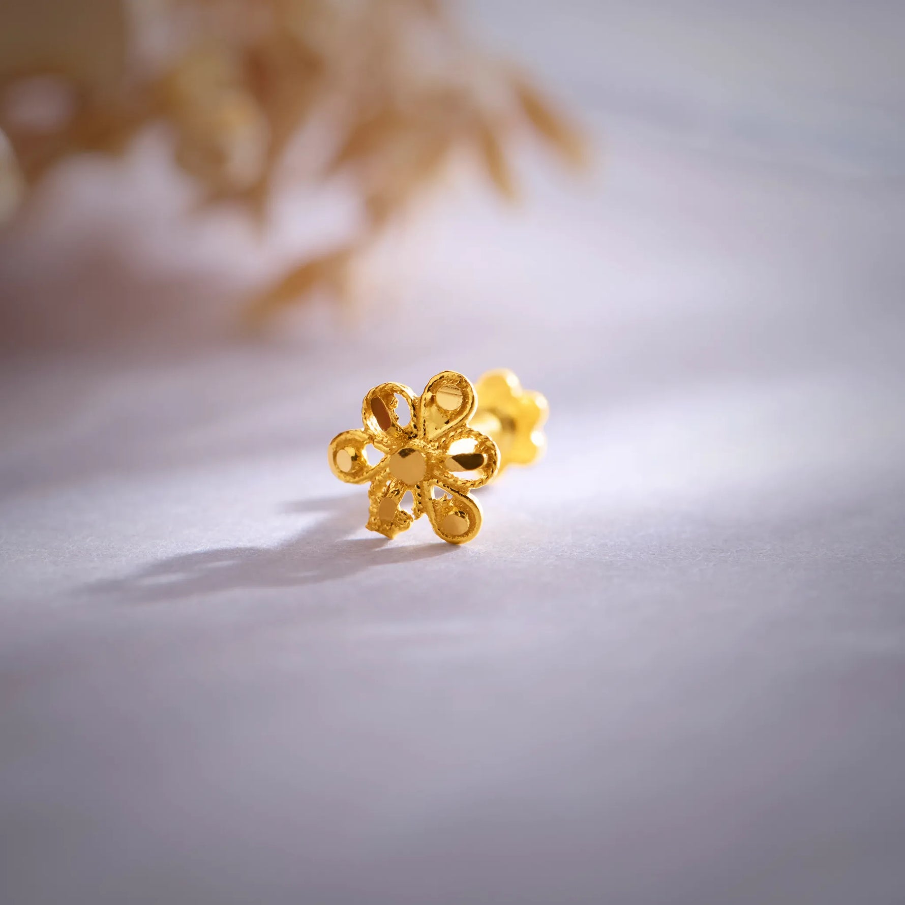 Close up of a floral 18K nose pin gold placed on a soft white surface highlighting intricate design and polished finish