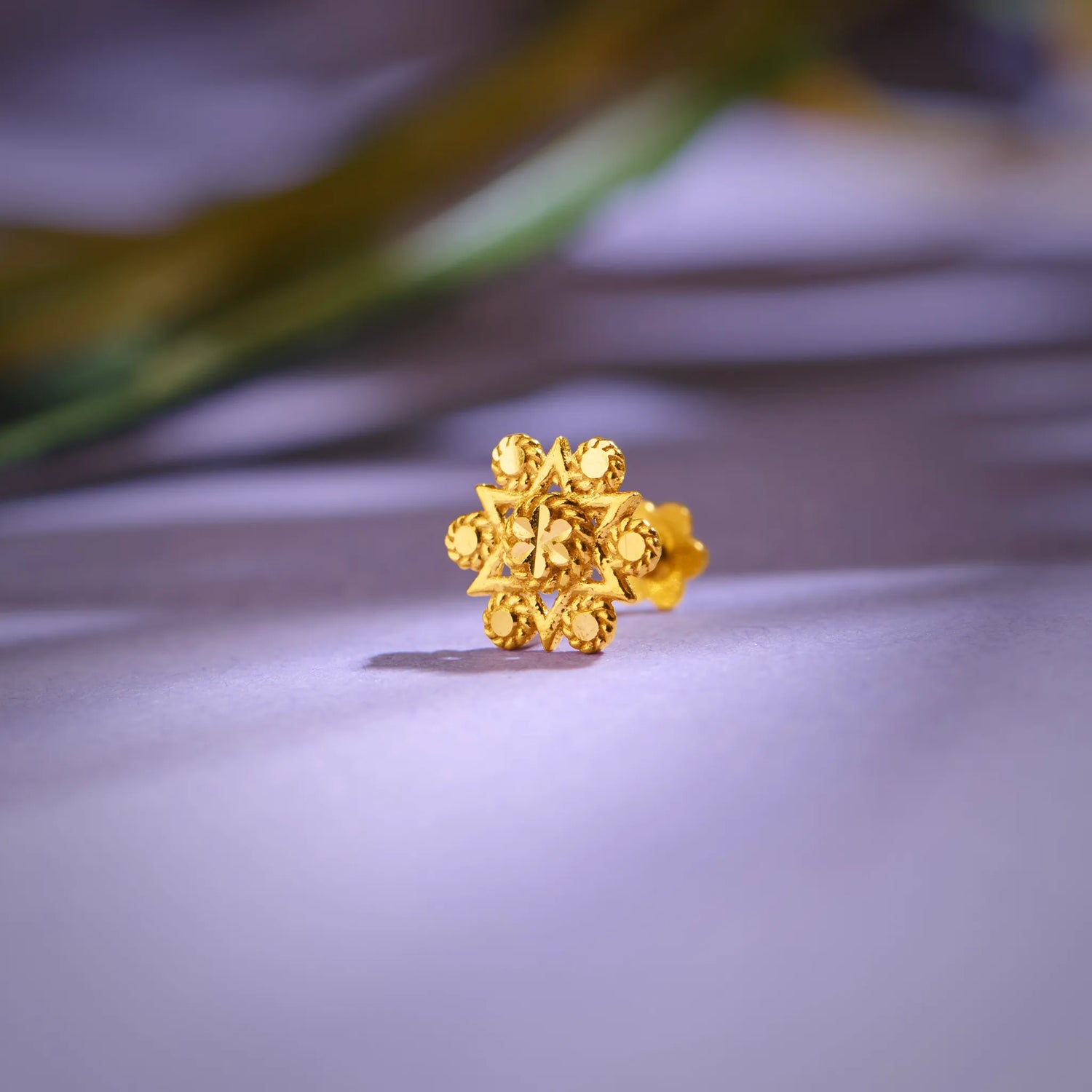 Floral cluster 18K nose pin gold placed on a soft lavender surface highlighting its detailed craftsmanship