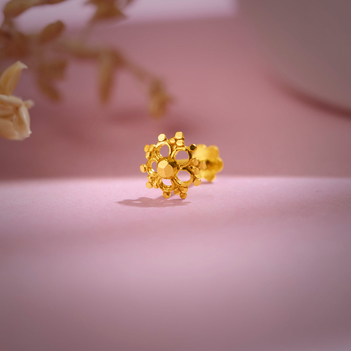 Artistic shot of floral 18K nose pin gold on a pink backdrop capturing its polished finish