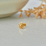 Close up of floral 18K gold nose pin placed on a white surface with soft decor elements highlighting intricate detailing