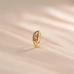 Close up of multicolour stone 18K gold nose ring standing upright on a soft beige fabric surface with gentle light reflections