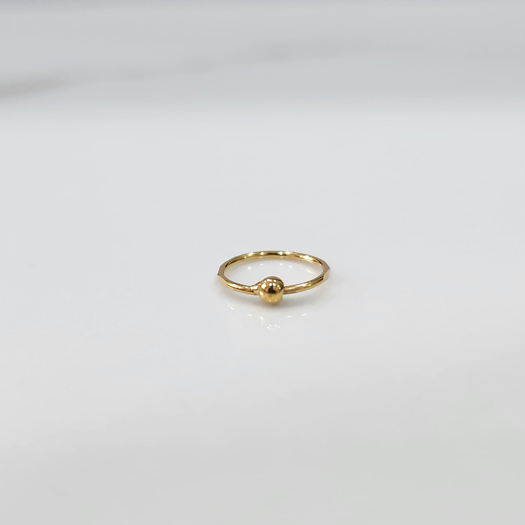 Close up of delicate open hoop gold nose ring placed flat on a white surface
