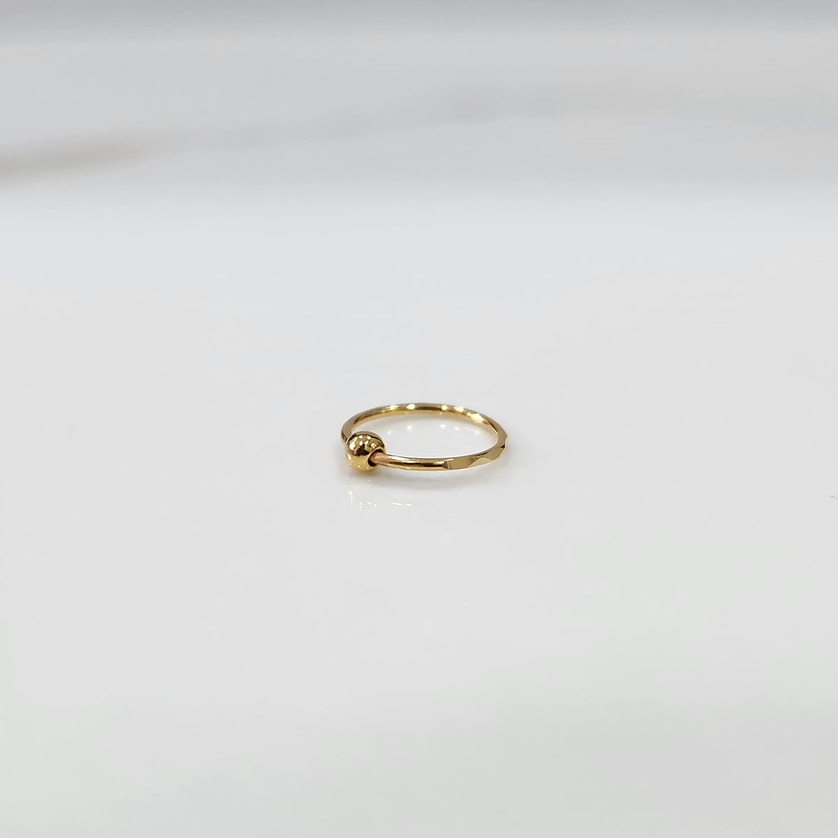 Alternate angle view of small open hoop gold nose ring on a white background showing clasp opening
