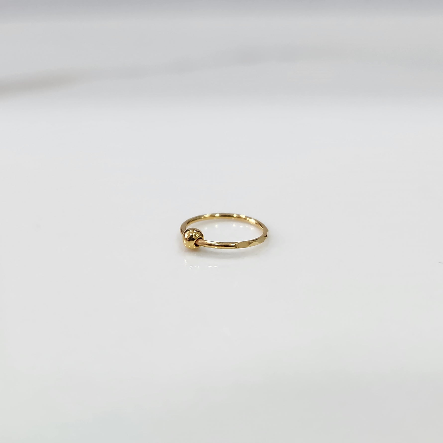 Alternate angle view of small open hoop gold nose ring on a white background showing clasp opening