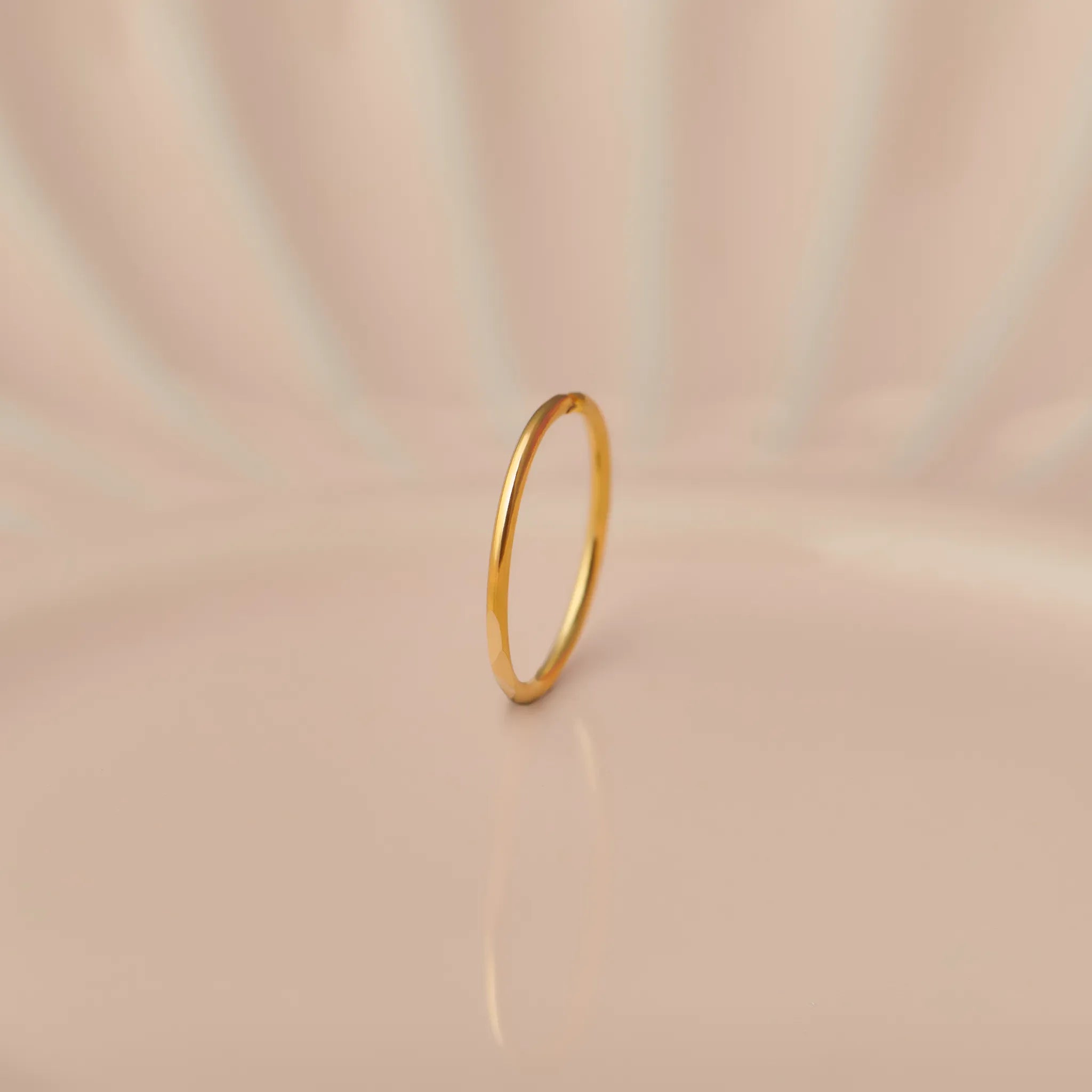 Front view of slim plain 18K gold hoop nose ring standing upright on a soft beige background with subtle light reflections