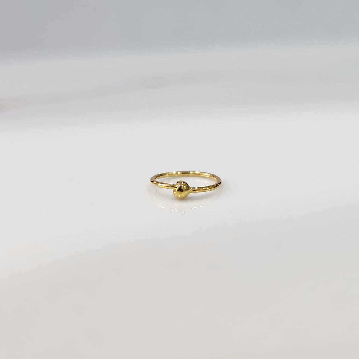 Close up of open hoop gold nose ring placed on a white background showing the clasp free open design