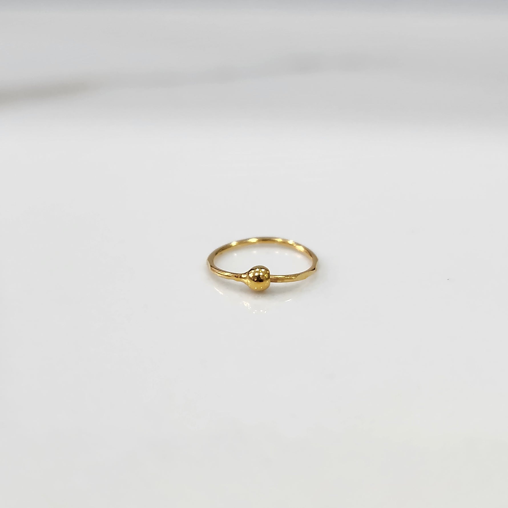 Top view of small open hoop 18K gold nose ring placed on a white background for size clarity