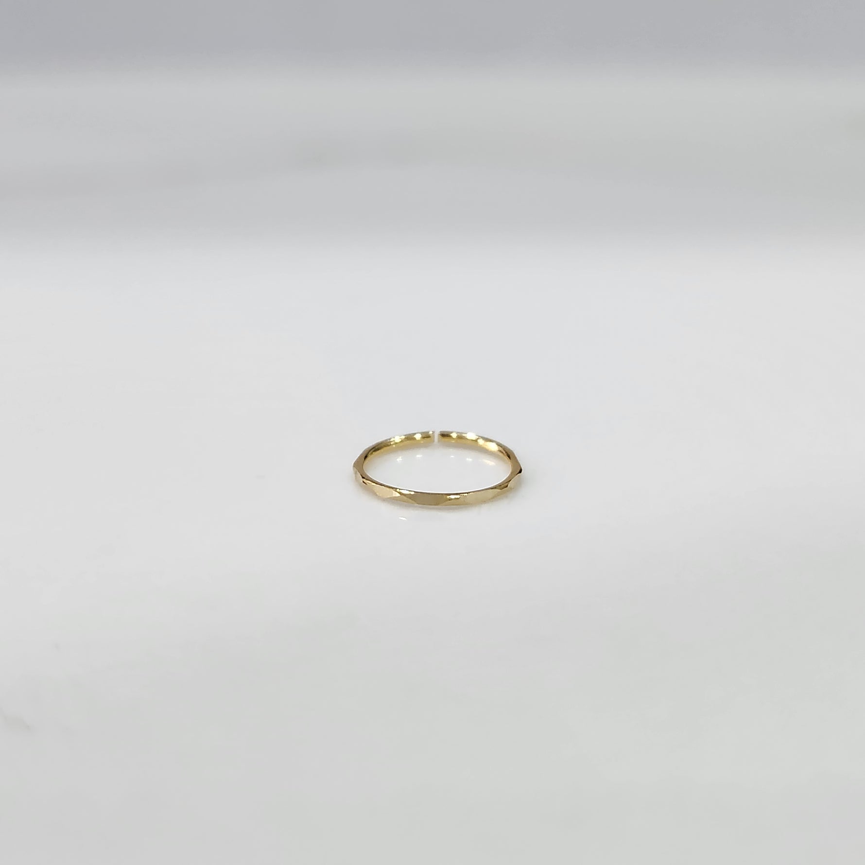 Top view of small plain gold hoop nose ring placed flat on a light grey surface to show actual size