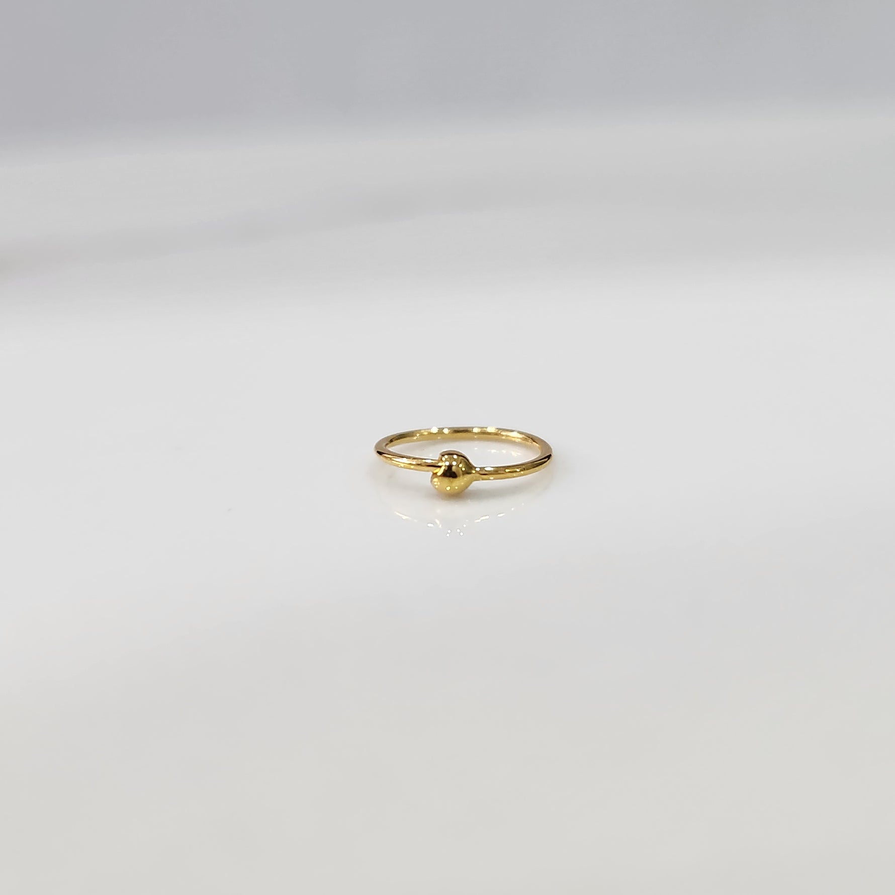 Flat lay view of small open hoop gold nose ring on a white surface showing its petite size