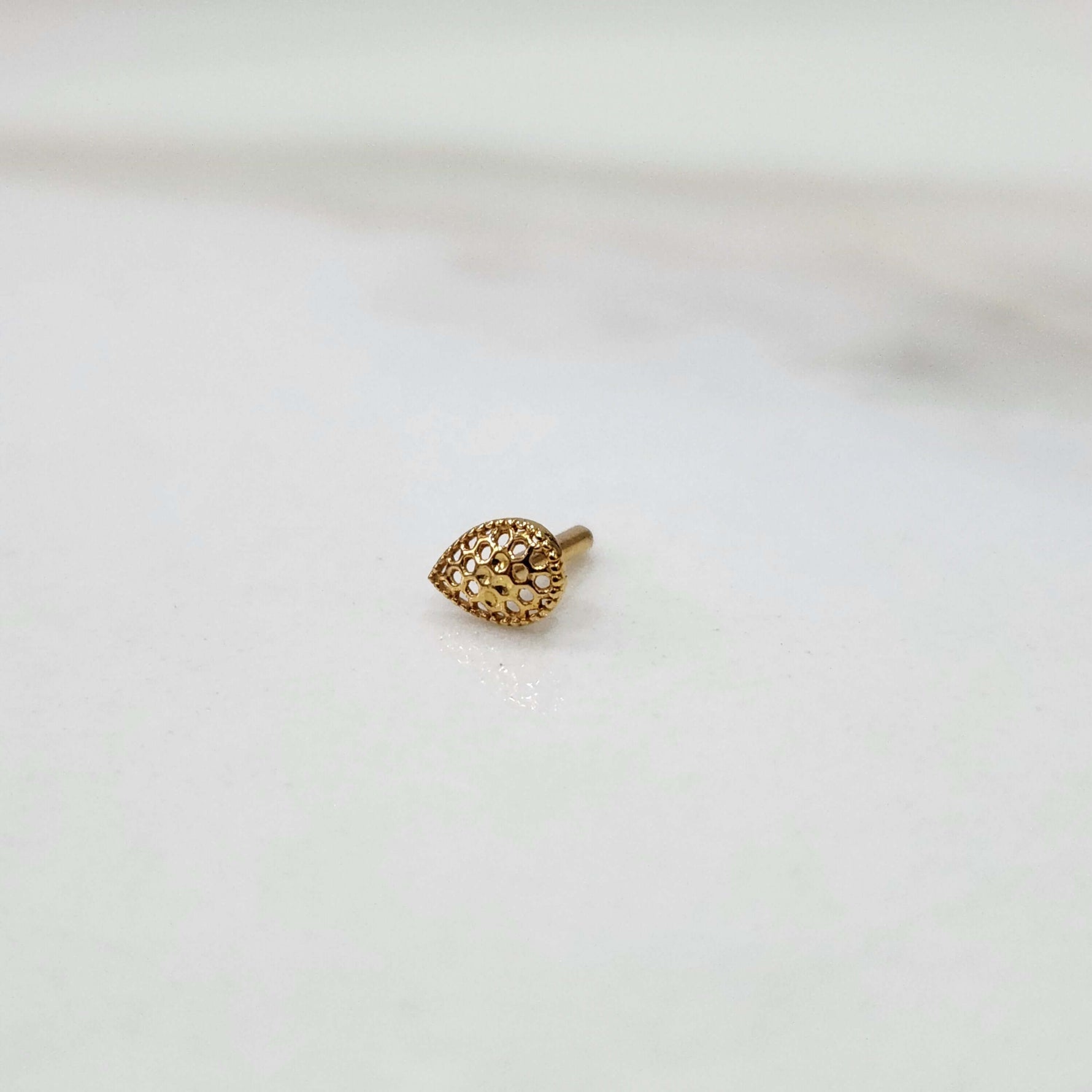 Close up of handcrafted teardrop gold nose pin design on white background elegant and modern in style